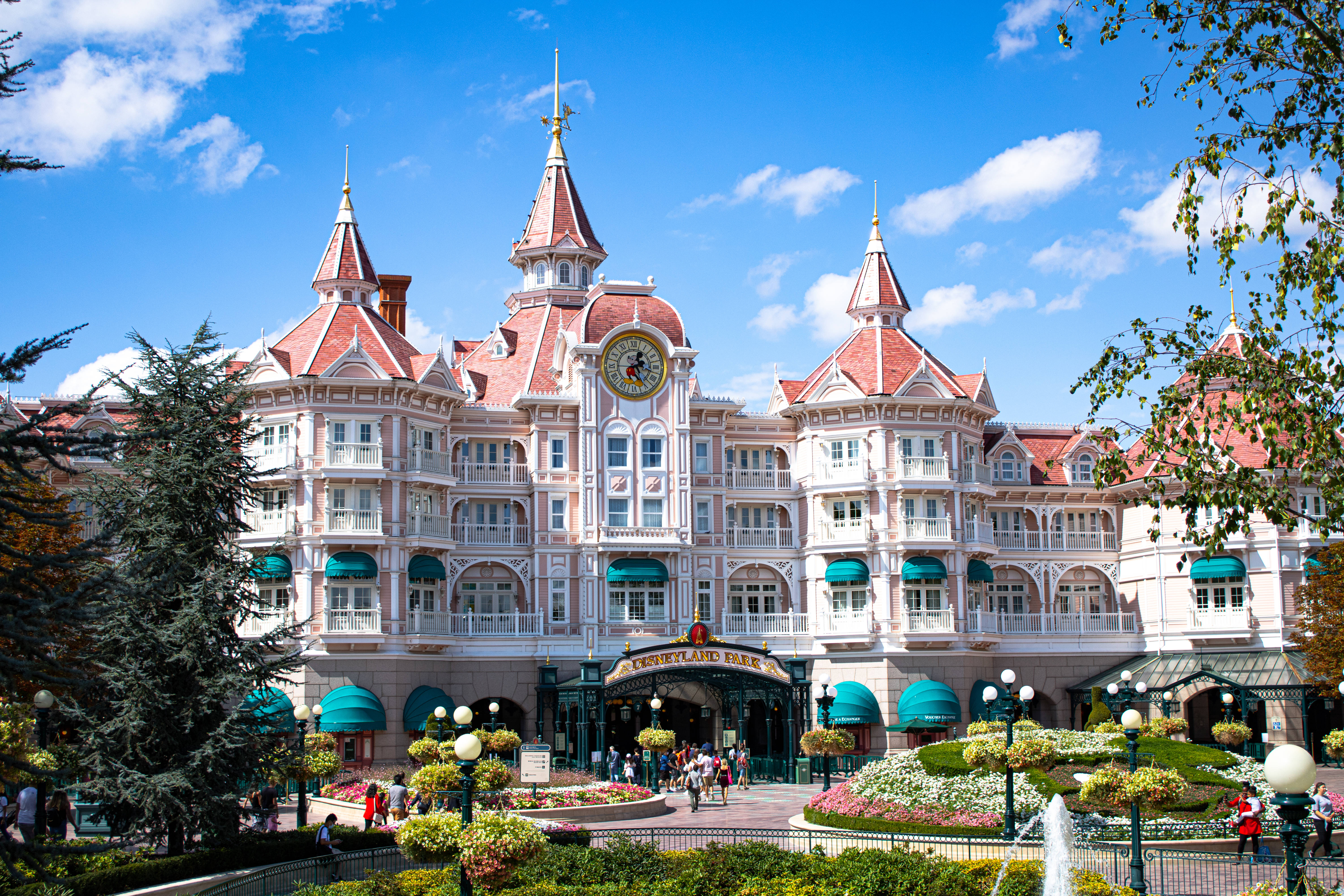 Disneyland Desktop 桌布 壁紙 — 宏偉的迪士尼風格城堡，紅色屋頂和綠色遮陽篷，在明亮的藍天和蓬鬆的雲朵下。