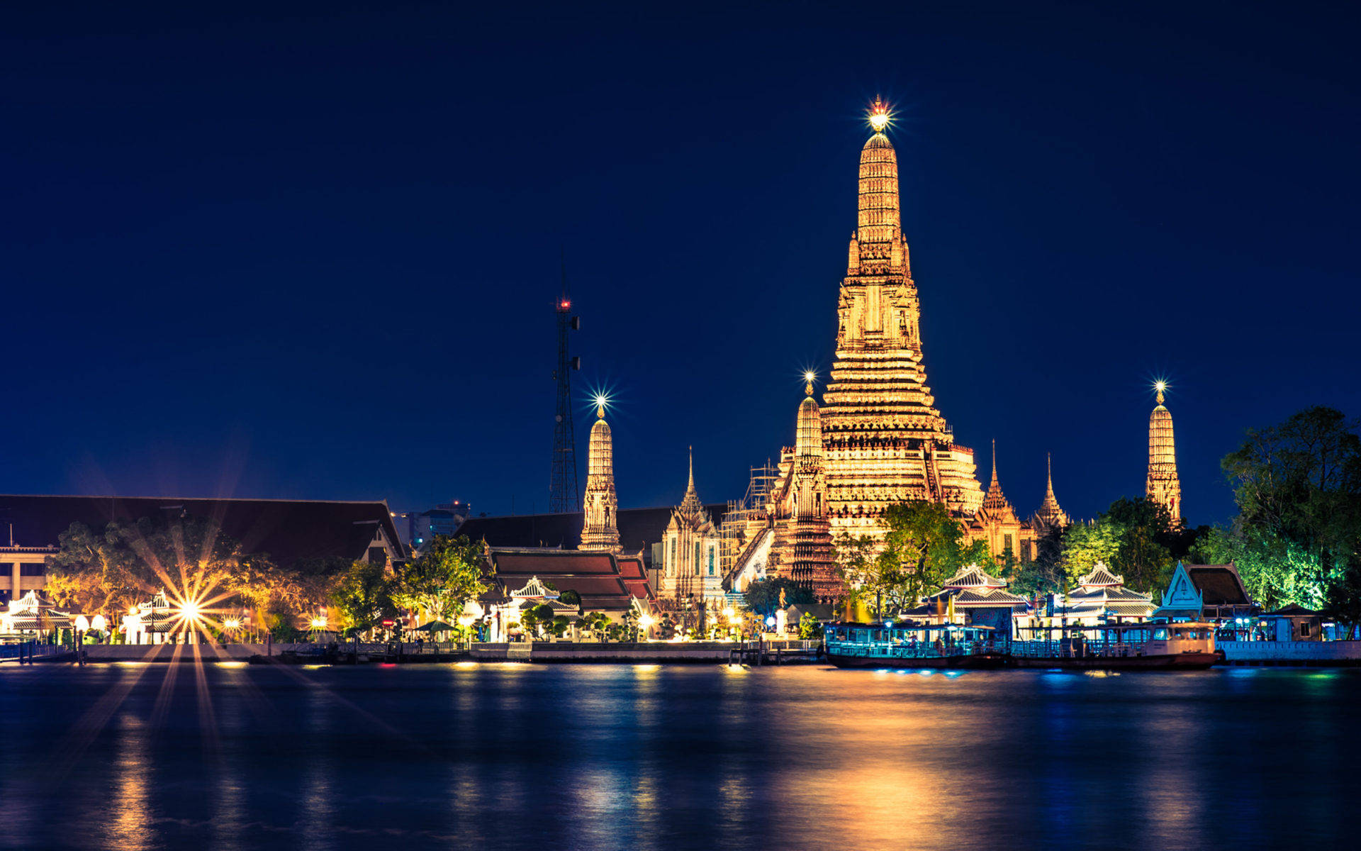 Bangkok 桌布 壁紙 — 宏偉的鄭王廟在深藍色夜空下閃耀金光，倒映在平靜的河水中，伴隨著星芒般的光點。