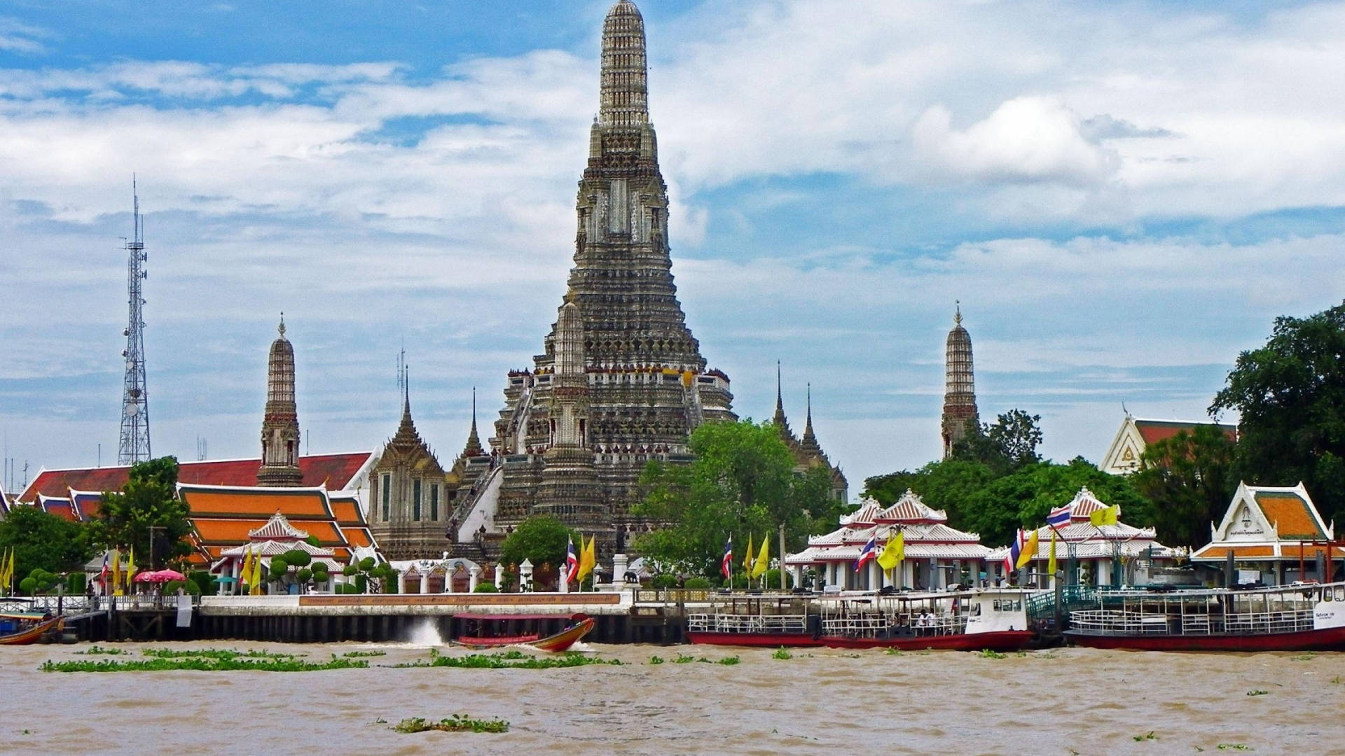 Bangkok 桌布 壁紙 — 宏偉的鄭王廟從河岸雄偉地聳立，下方停泊著船隻，天空部分多雲。