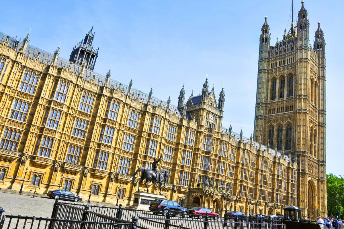 House Of Parliament 桌布 壁紙 — 宏偉的金色哥德式威斯敏斯特宮，附有伊麗莎白塔和騎馬雕像，在清澈的藍天下。