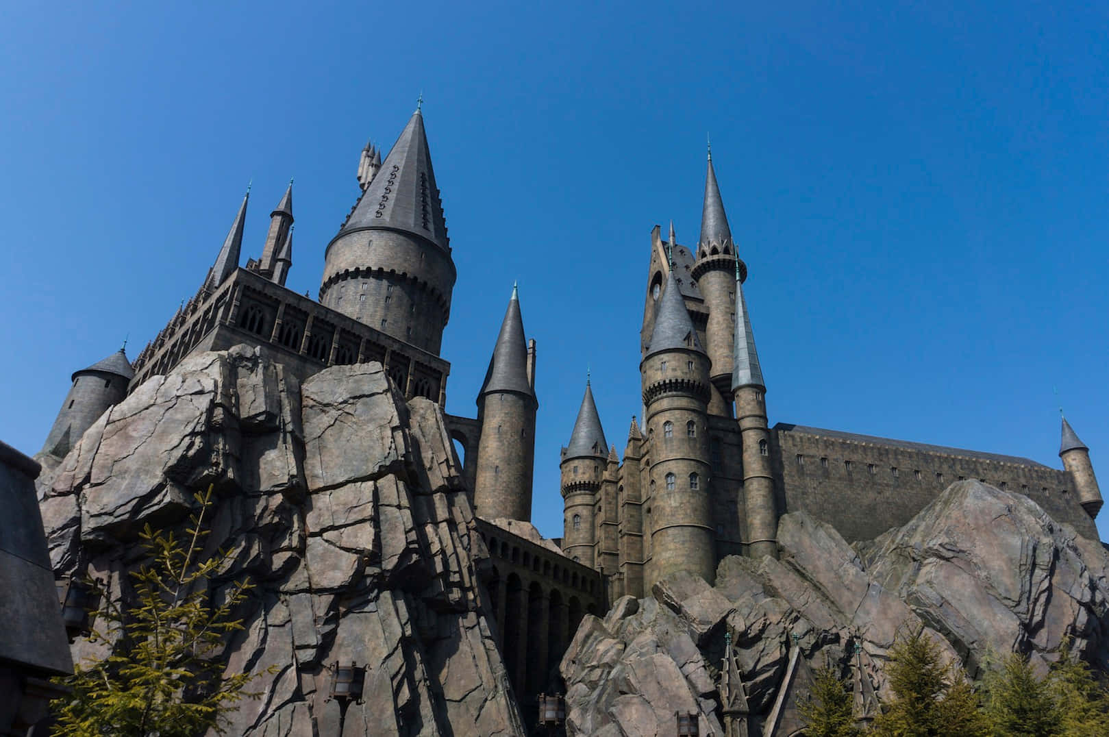 Wizarding World 桌布 壁紙 — 宏偉的霍格華茲城堡坐落在崎嶇的懸崖上，在清澈的藍天下，擁有尖銳的尖頂和石塔。