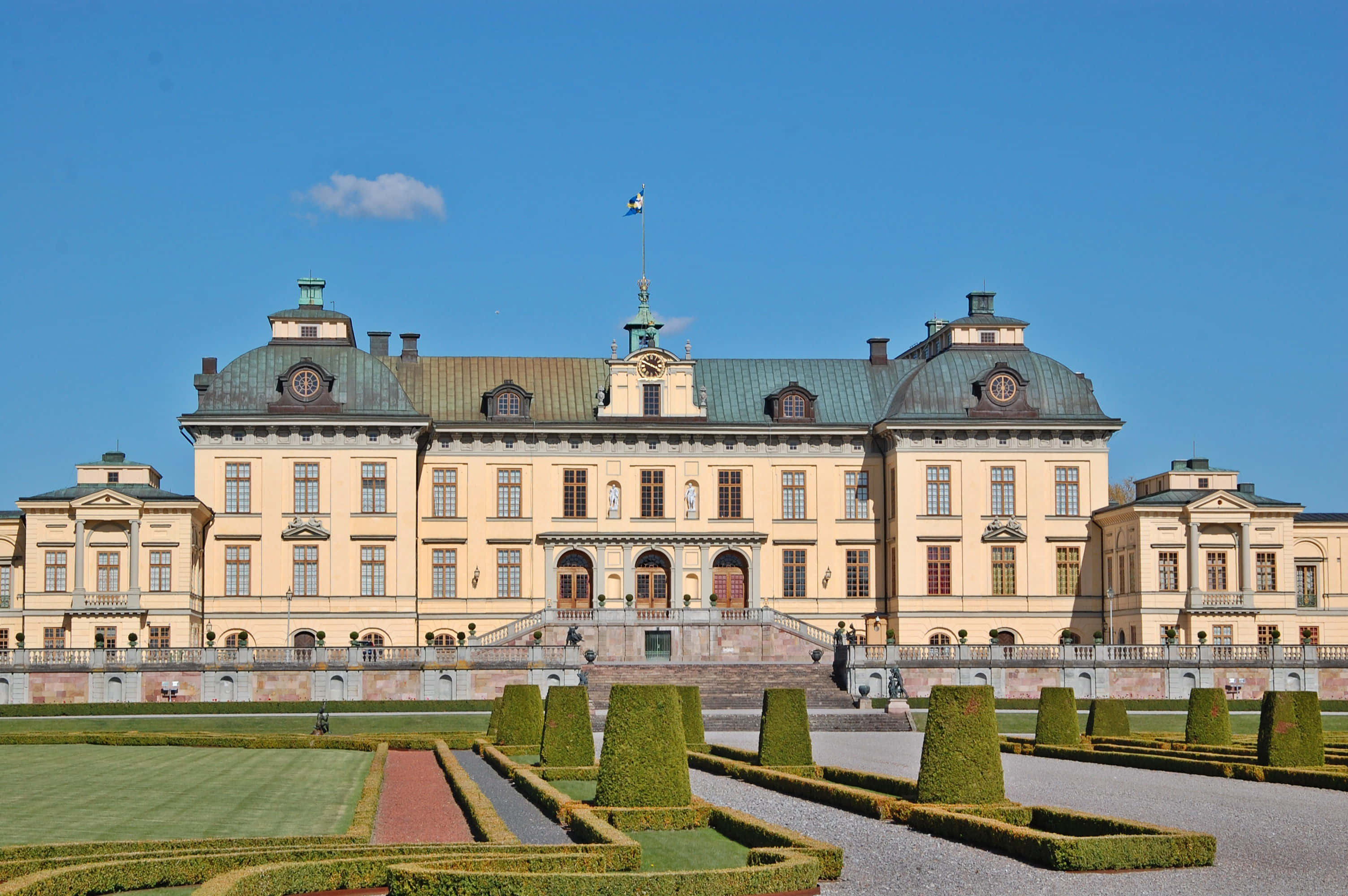 Drottningholm Palace 桌布 壁紙 — 宏偉的黃色宮殿，擁有綠色圓頂和對稱花園，在清澈的藍天下。