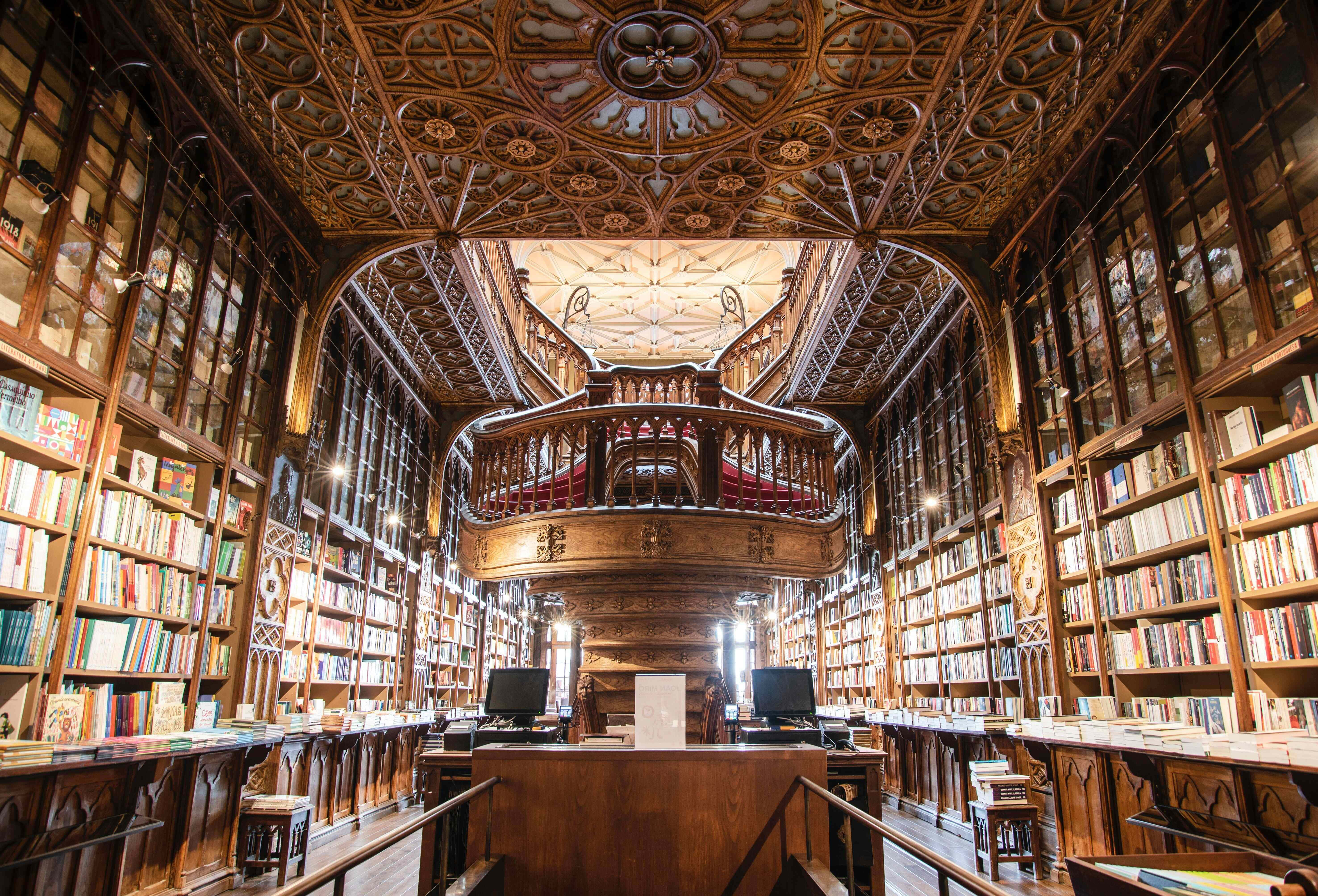 The Hogwarts Library 桌布 壁紙 — 宏偉華麗的圖書館，擁有高聳的木製書架、精緻的方格天花板，以及沐浴在溫暖金色光線中的中央螺旋樓梯。