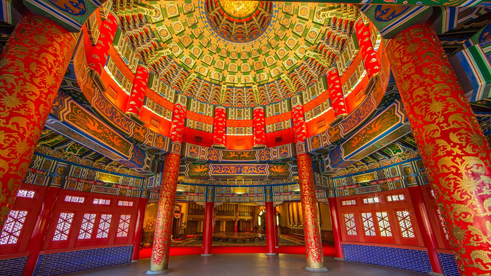 中國 桌布 壁紙 — 宏偉華麗的寺廟內部，擁有高聳的紅色柱子、金色鏤雕，以及裝飾著複雜圖案和溫暖燈光的耀眼多層天花板。