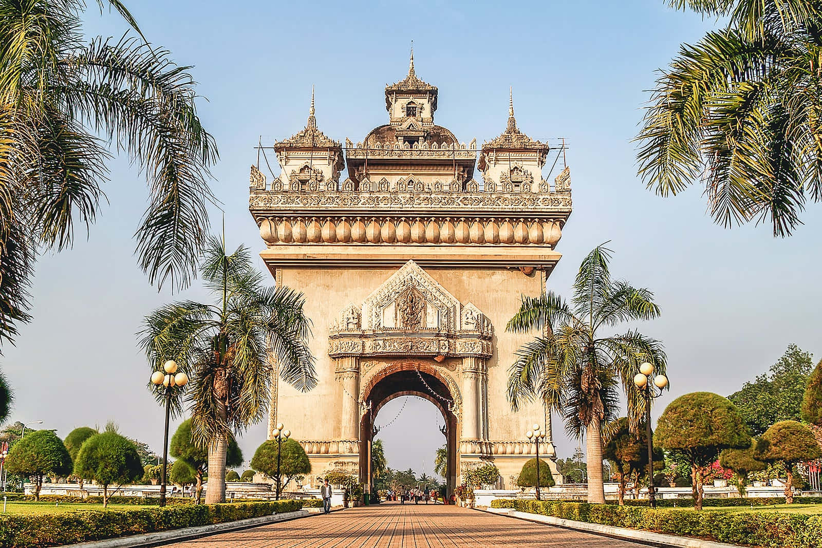 Laos 桌布 壁紙 — 宏偉華麗的拱門，兩旁棕櫚樹襯托，在清澈藍天下，一條鋪砌步道穿過其中。