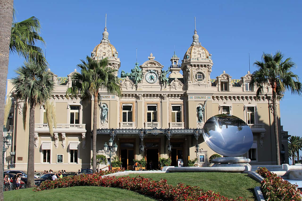 Casino 桌布 壁紙 — 宏偉華麗的賭場建築，棕櫚樹和反光球體雕塑，在晴朗的藍天下。