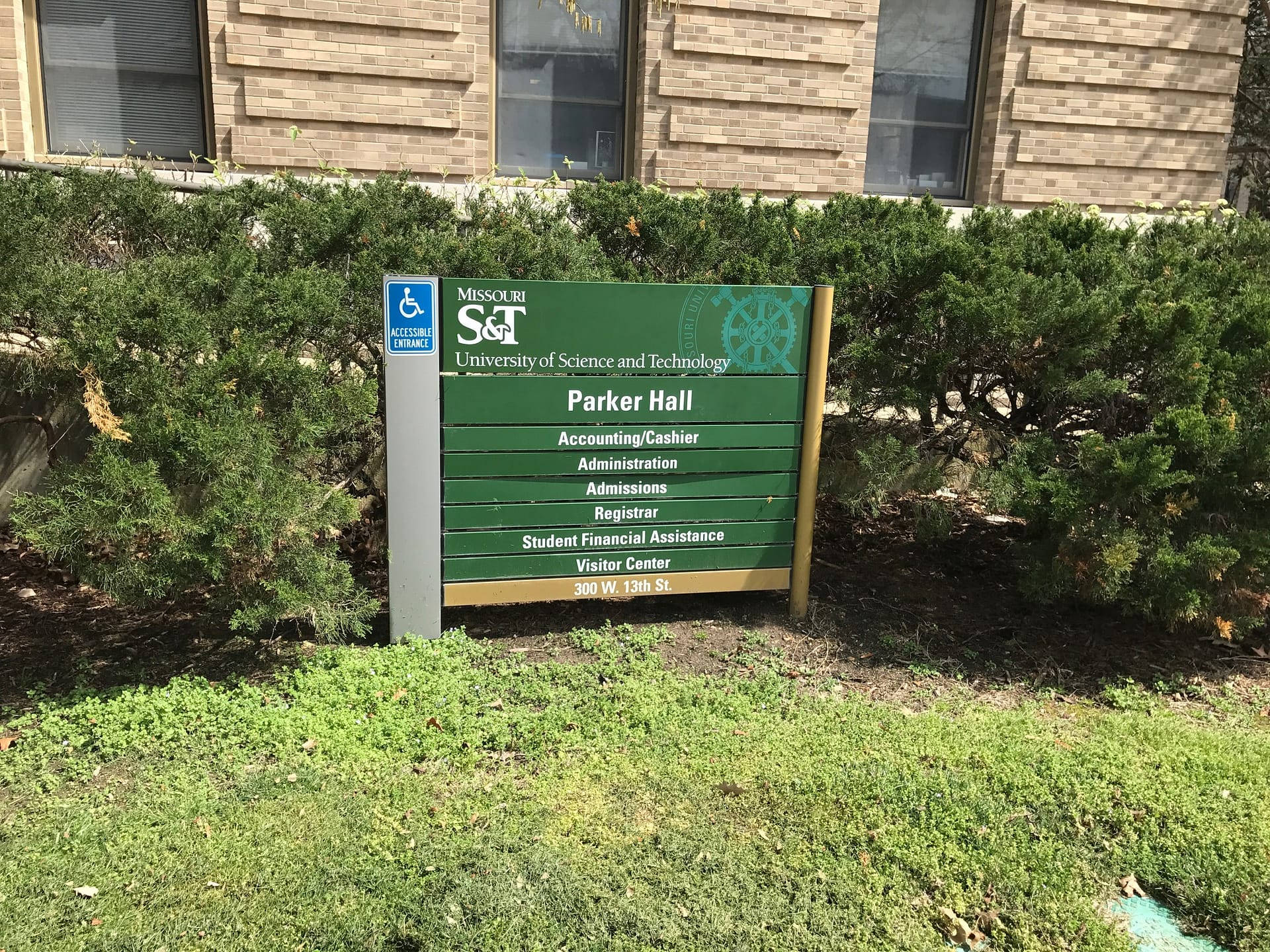 學校 桌布 壁紙 — 密蘇里科技大學帕克廳的綠色標誌矗立在磚砌建築前，周圍環繞著綠色灌木和草地。