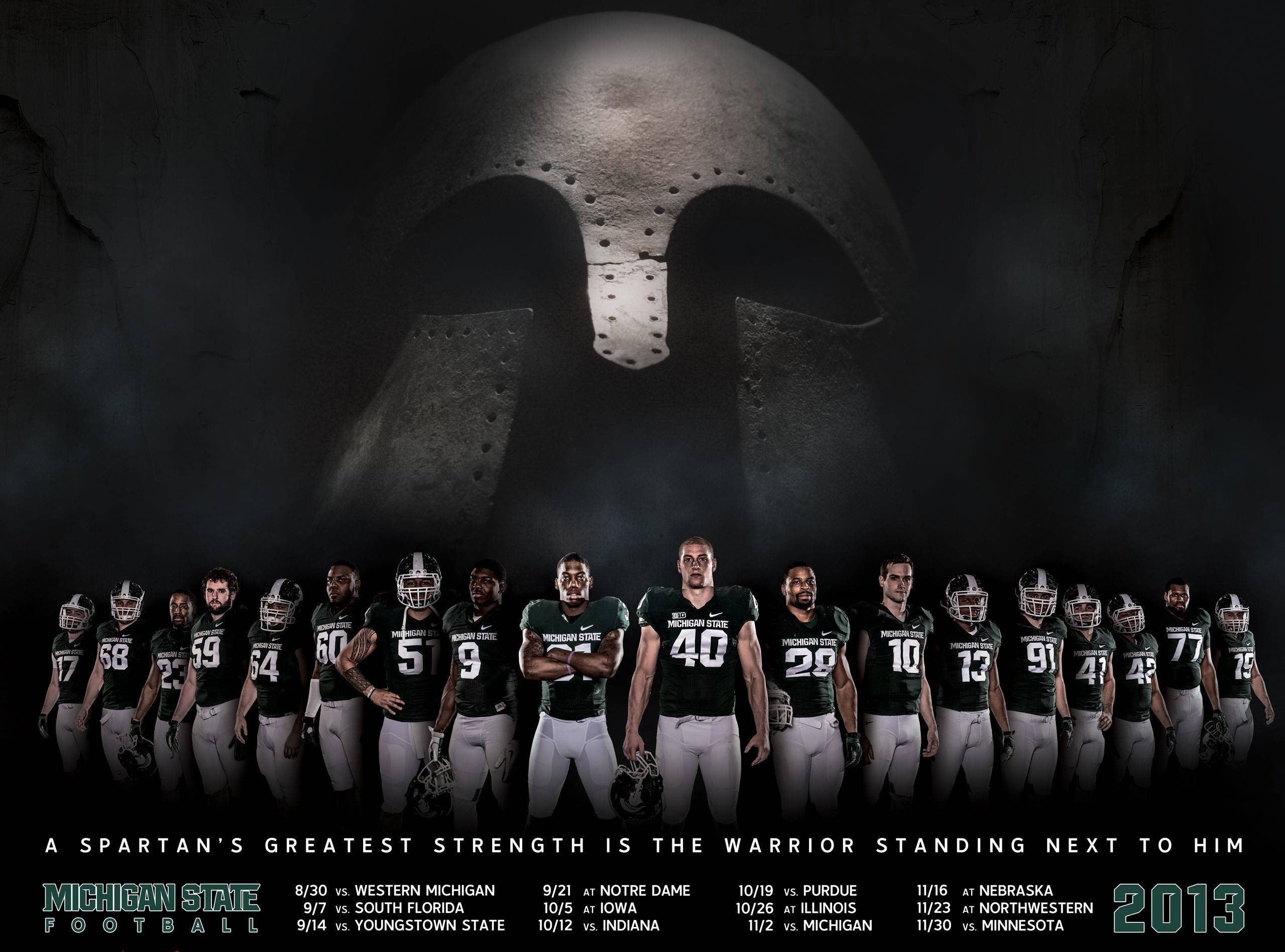 Michigan State Spartans 桌布 壁紙 — 密西根州立大學足球隊穿著綠色球衣，站在一個巨大的斯巴達頭盔前，背景是黑暗的洞穴般環境。