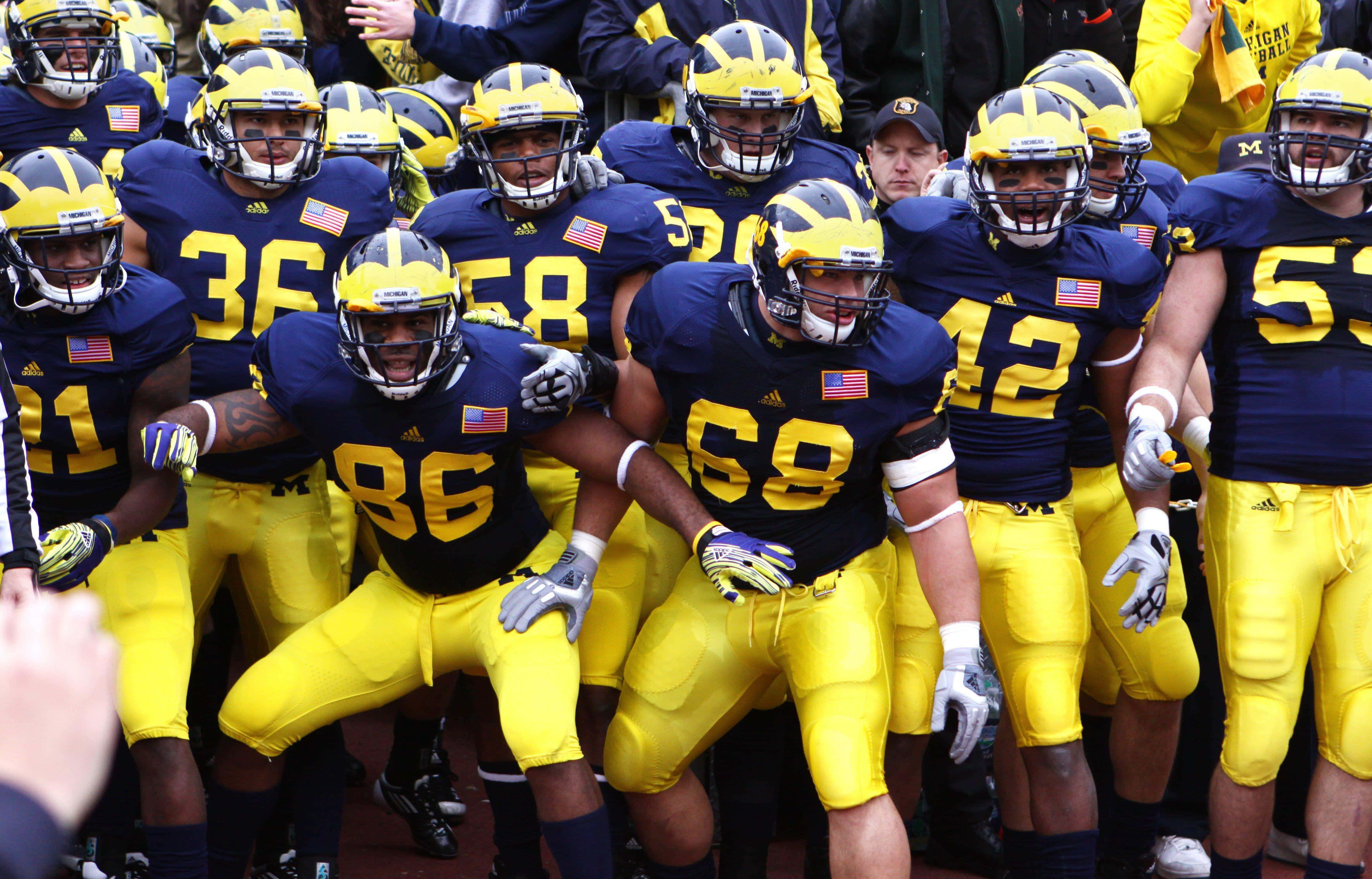 Michigan Football 桌布 壁紙 — 密西根狼獾隊的足球員身穿海軍藍和黃色裝備，在比賽前激烈地聚在一起。