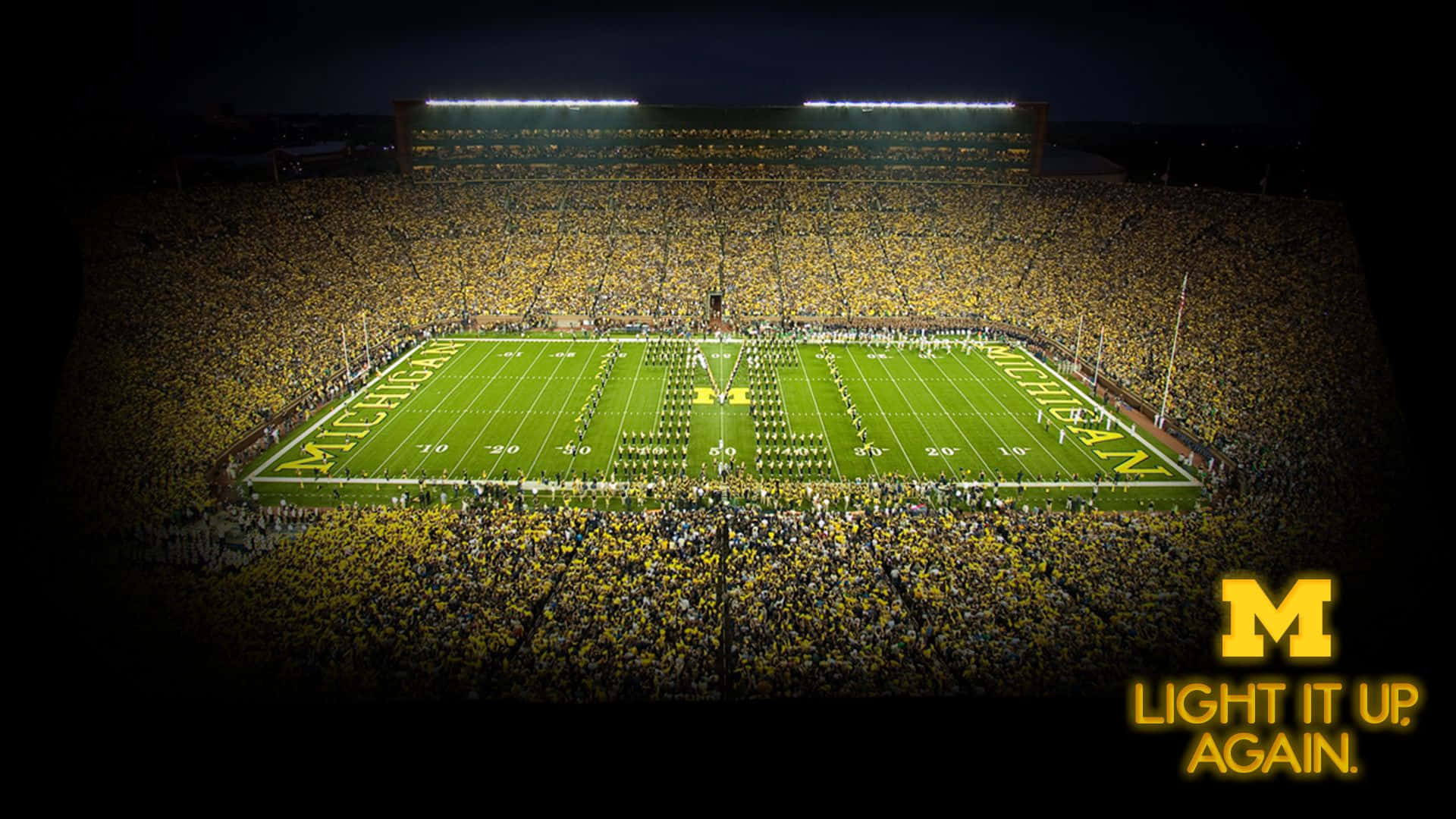 Michigan Wolverines 桌布 壁紙 — 密西根體育場夜晚的鳥瞰圖，黃色衣服的熱情球迷在明亮的體育場燈光下歡呼。
