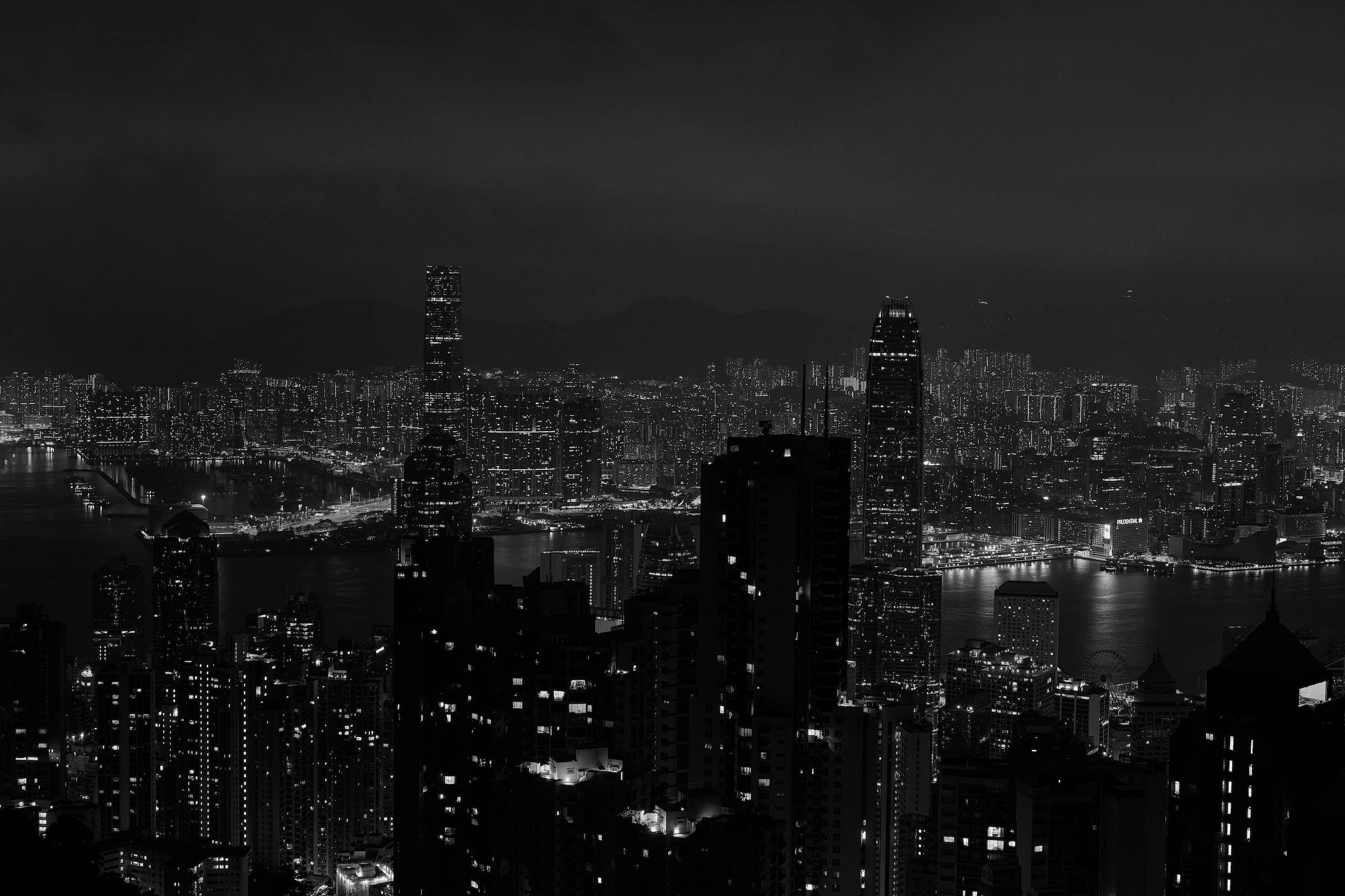 Night Aesthetic 桌布 壁紙 — 密集城市天際線的單色夜景，帶有發光的窗戶和一條黑暗的水道穿過城市景觀。