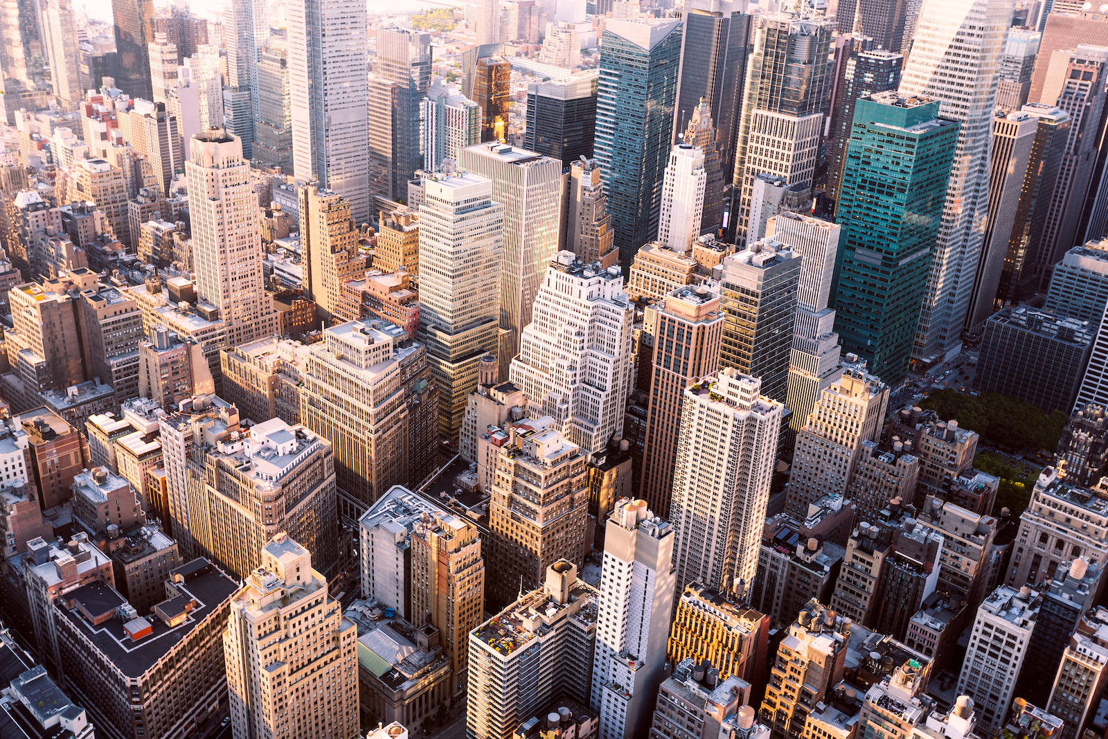 New York 桌布 壁紙 — 密集城市天際線的鳥瞰圖，沐浴在金色日出光中，光線從玻璃摩天大樓和鋼鐵建築反射出來。