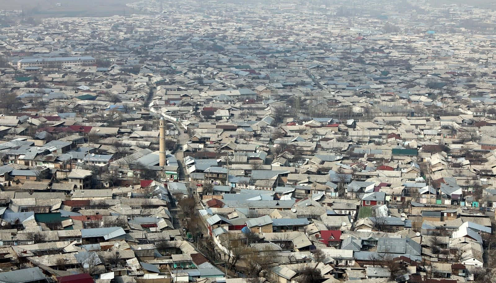 Kyrgyzstan 桌布 壁紙 — 密集城市擴張的鳥瞰圖，房屋緊密排列，一座突出的宣禮塔聳立在屋頂之上。