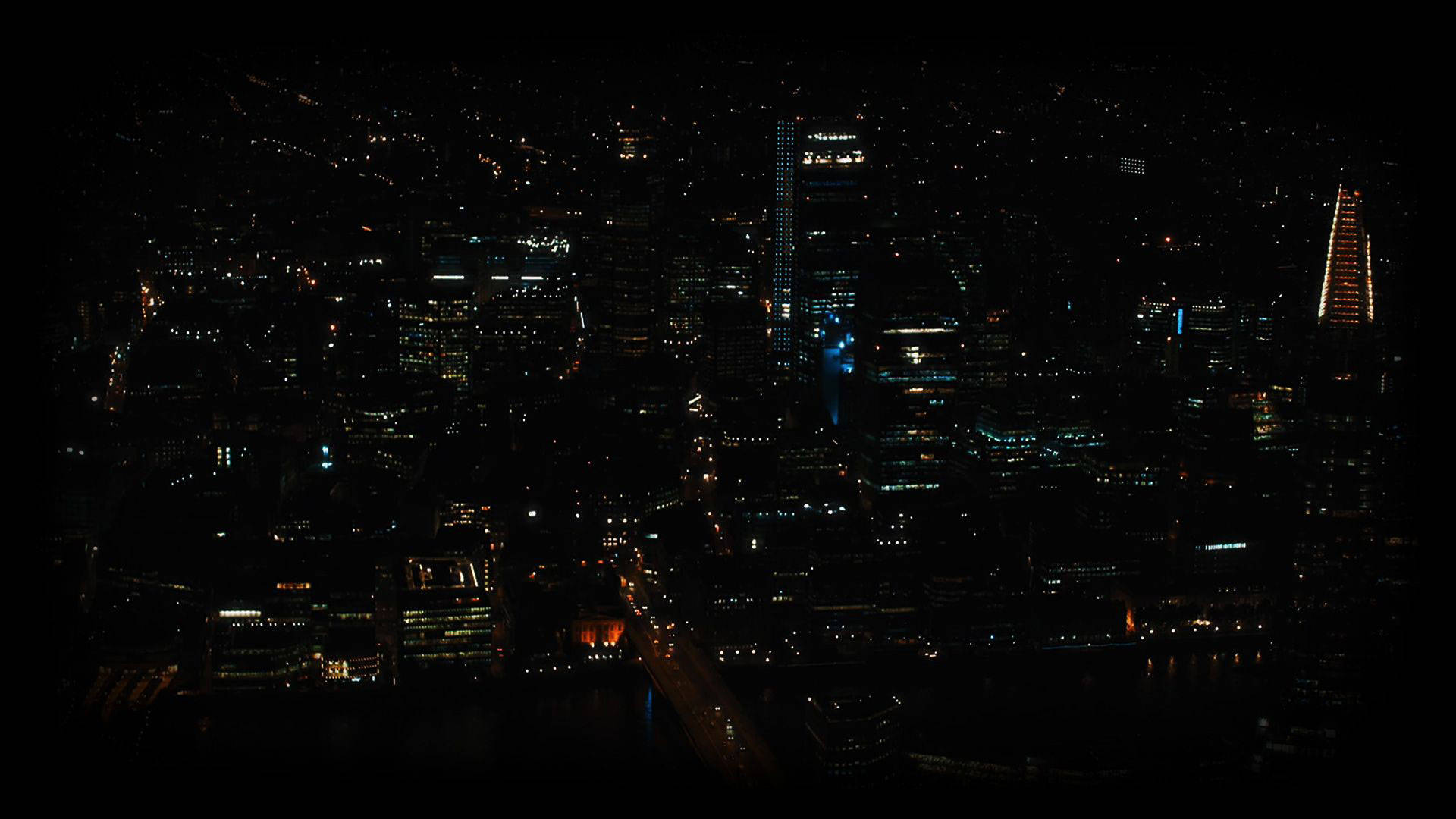 City At Night 桌布 壁紙 — 密集城市景觀的夜間鳥瞰圖，摩天大樓和街道在黑暗的天空下閃閃發光。