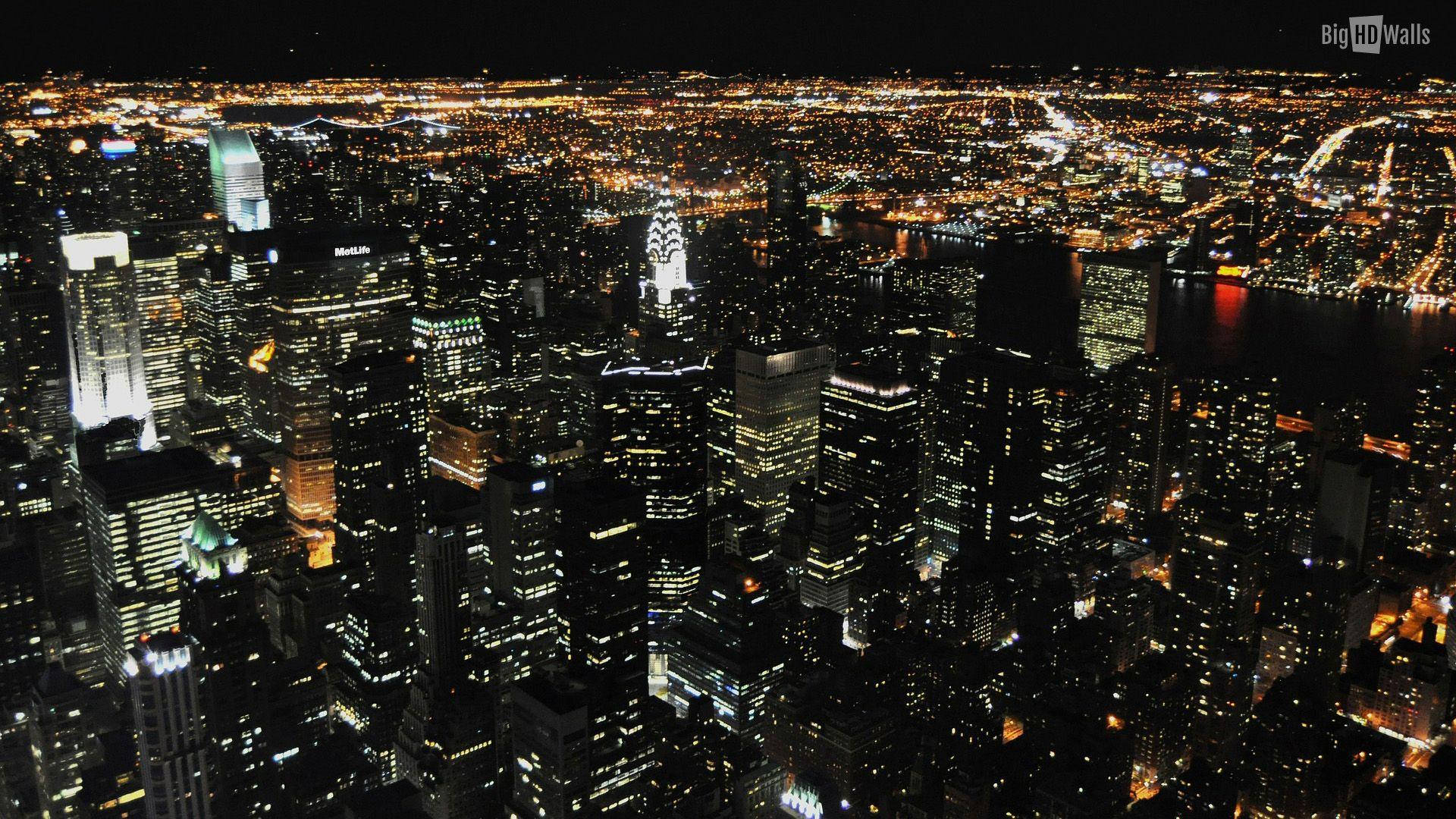 New York 桌布 壁紙 — 密集城市景觀的夜間鳥瞰圖，閃爍的摩天大樓和燈火通明的街道延伸向海濱。