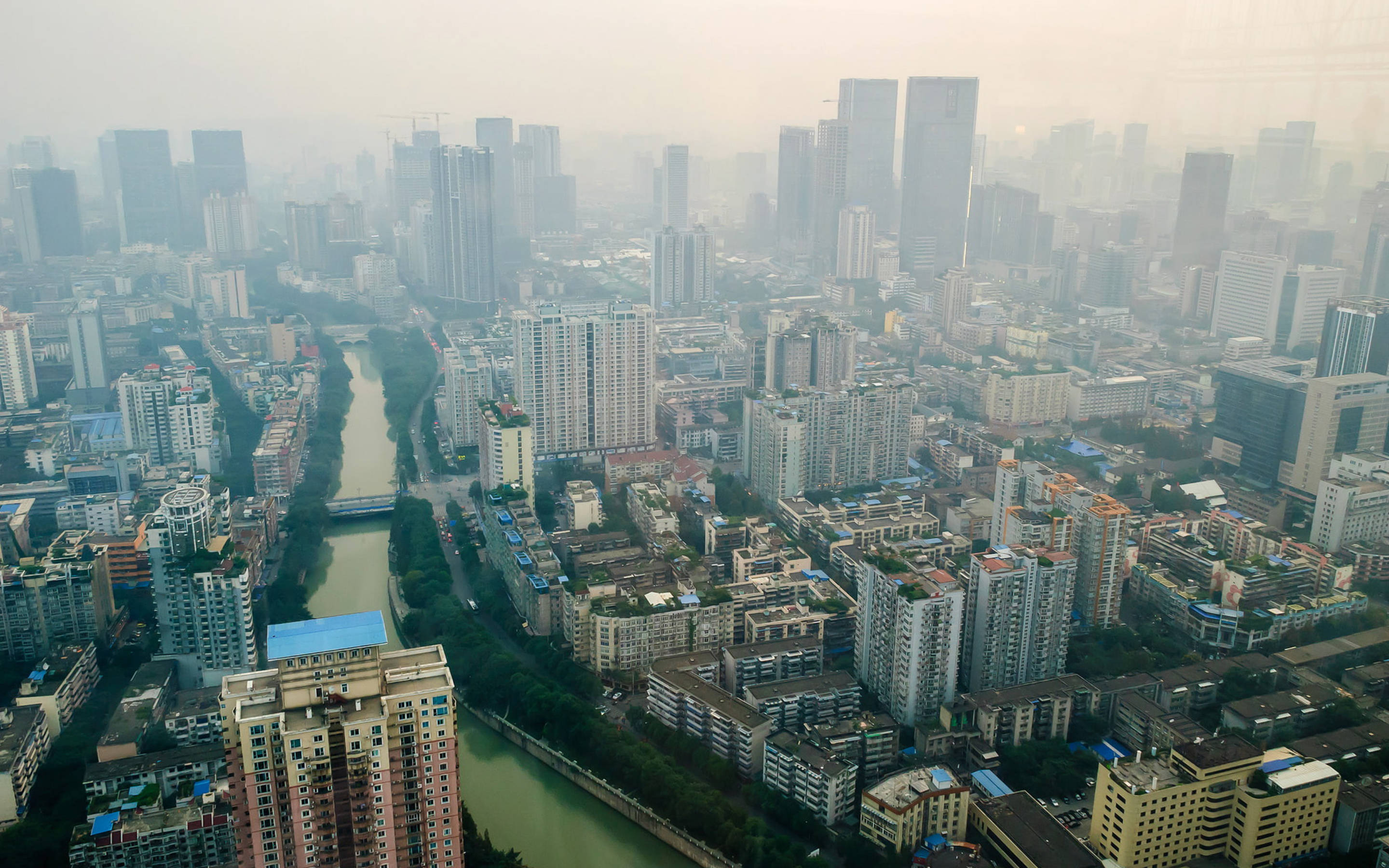 Chengdu 桌布 壁紙 — 密集城市景觀的朦朧鳥瞰圖，高聳的摩天大樓和蜿蜒的河流穿過混凝土叢林。