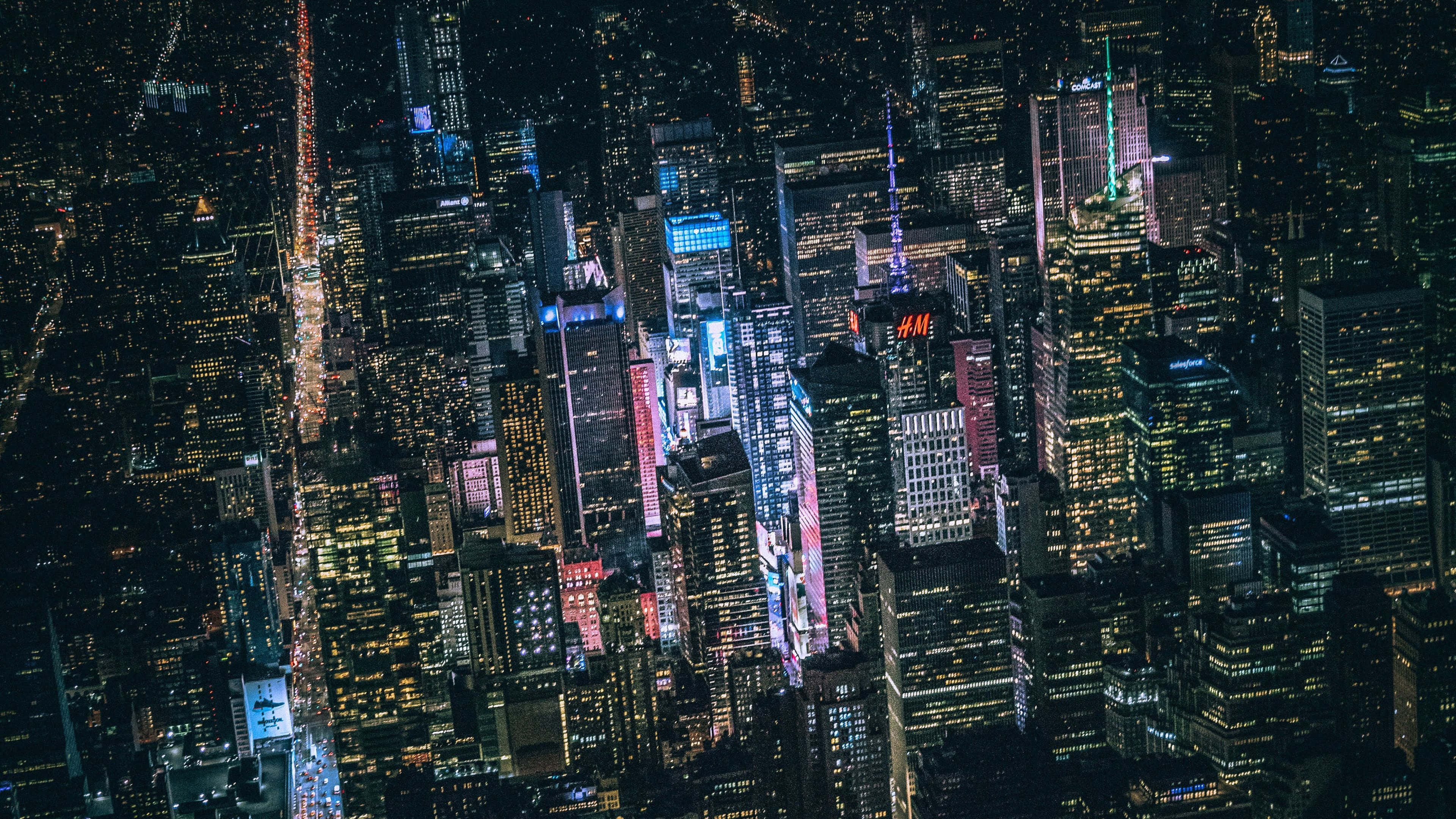 風景 桌布 壁紙 — 密集城市景觀的鳥瞰圖，夜晚時分，高聳的摩天大樓閃爍著色彩繽紛的霓虹燈和明亮的窗戶。