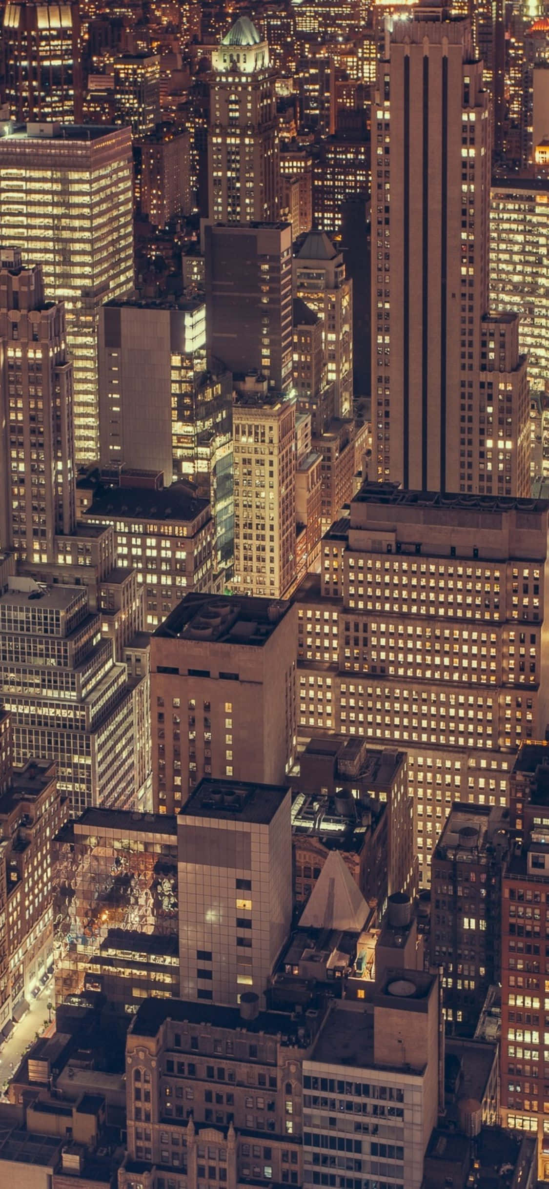 iPhone X New York 桌布 壁紙 — 密集城市景觀的鳥瞰圖，夜晚無數亮著的窗戶在黑暗的摩天大樓中溫暖地發光。