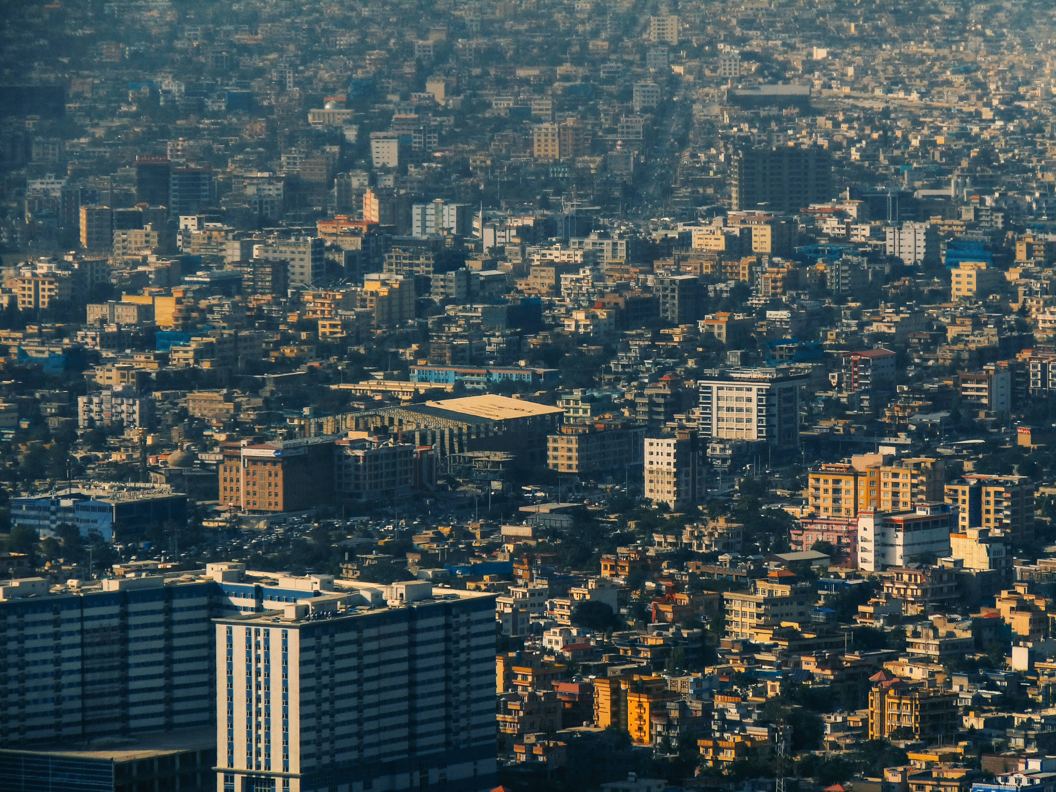 Kabul 桌布 壁紙 — 密集城市景觀的鳥瞰圖，溫暖的金色陽光穿過薄霧照射。