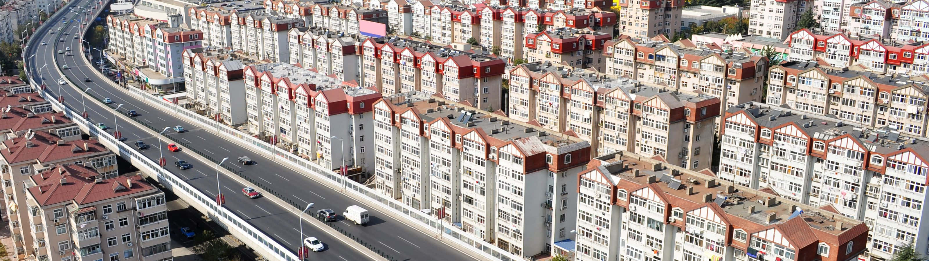 3200x900 桌布 壁紙 — 密集城市社區的鳥瞰圖，擁有統一的公寓樓群和一條彎曲且車流密集的高速公路。