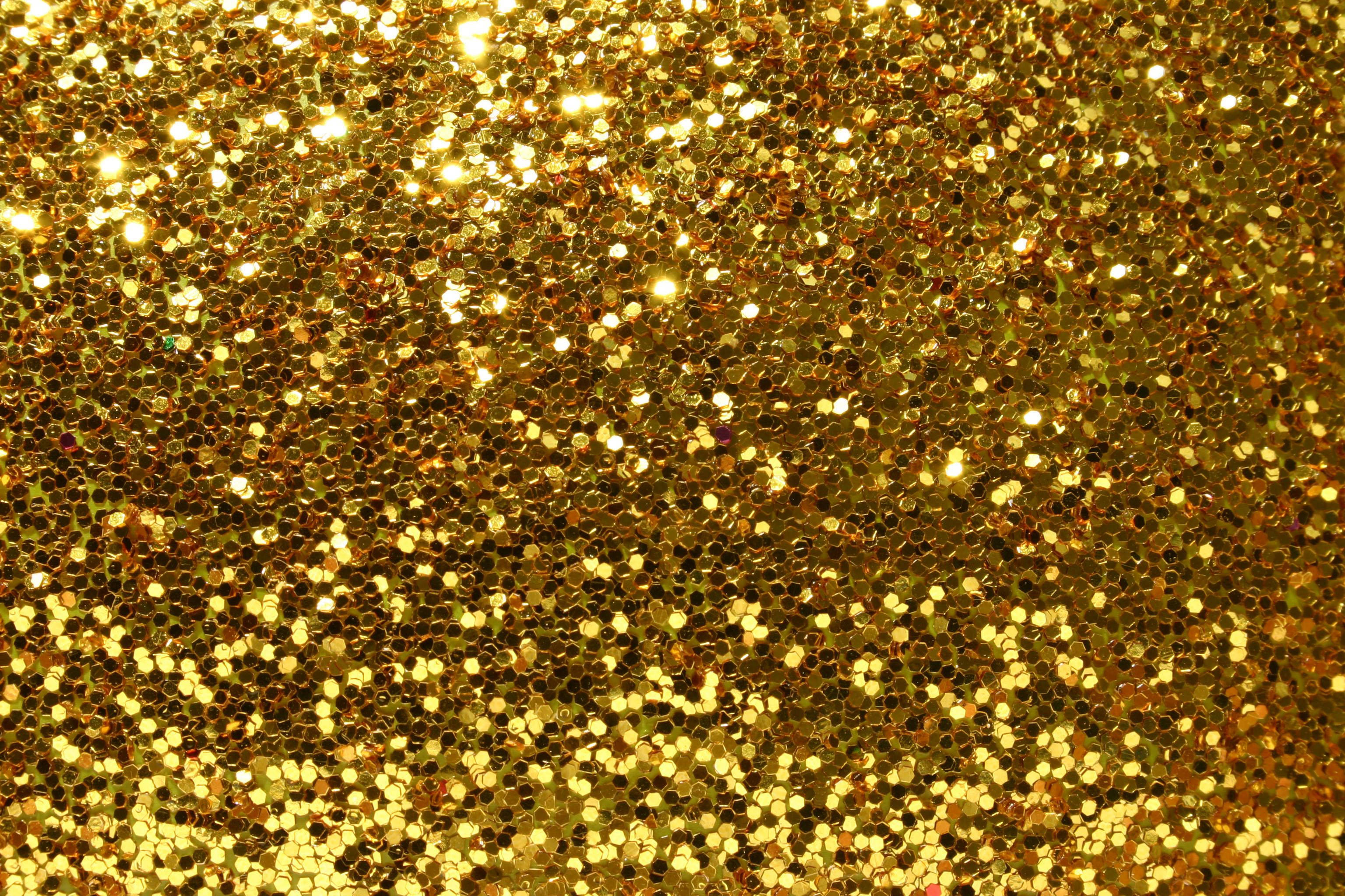 Gold Glitter 桌布 壁紙 — 密集的金色閃粉顆粒在紋理閃爍的表面上捕捉明亮光線。