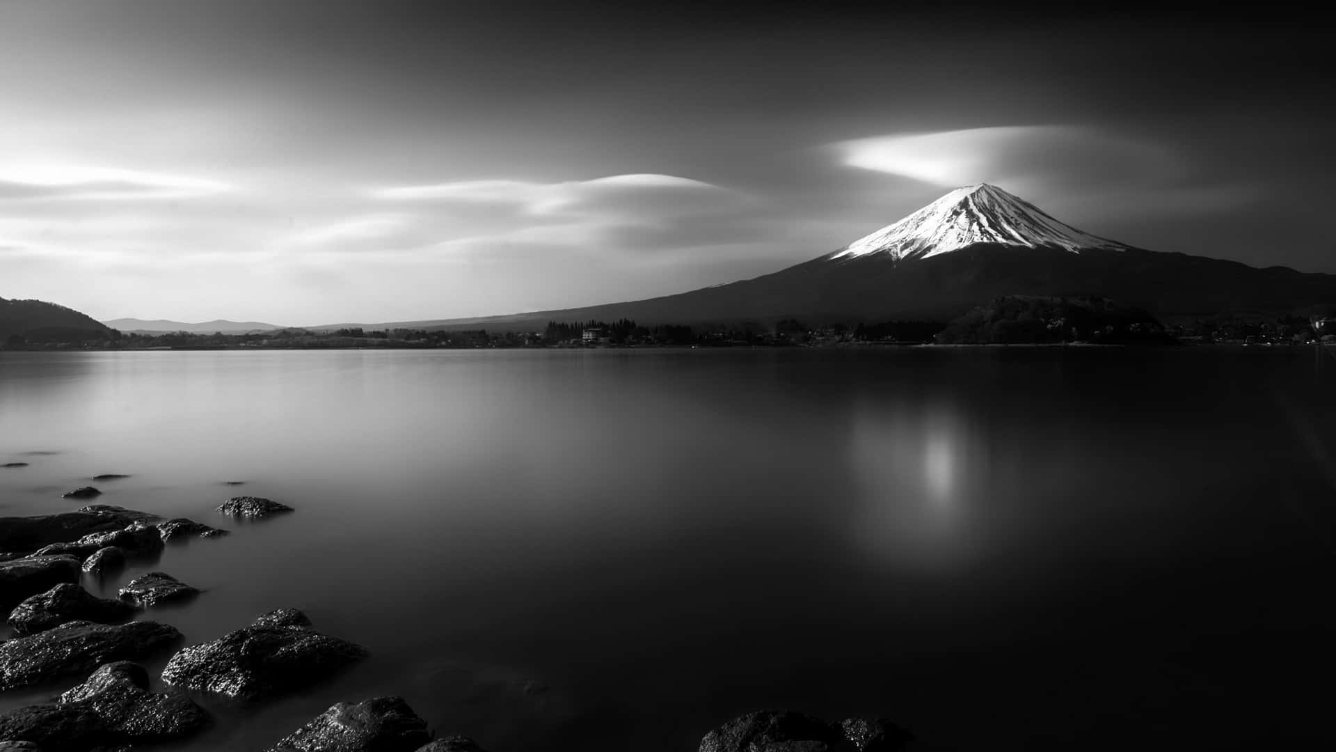 日本黑白 桌布 壁紙 — 富士山在平靜水面上的單色長曝光倒影，上方有戲劇性的雲層。