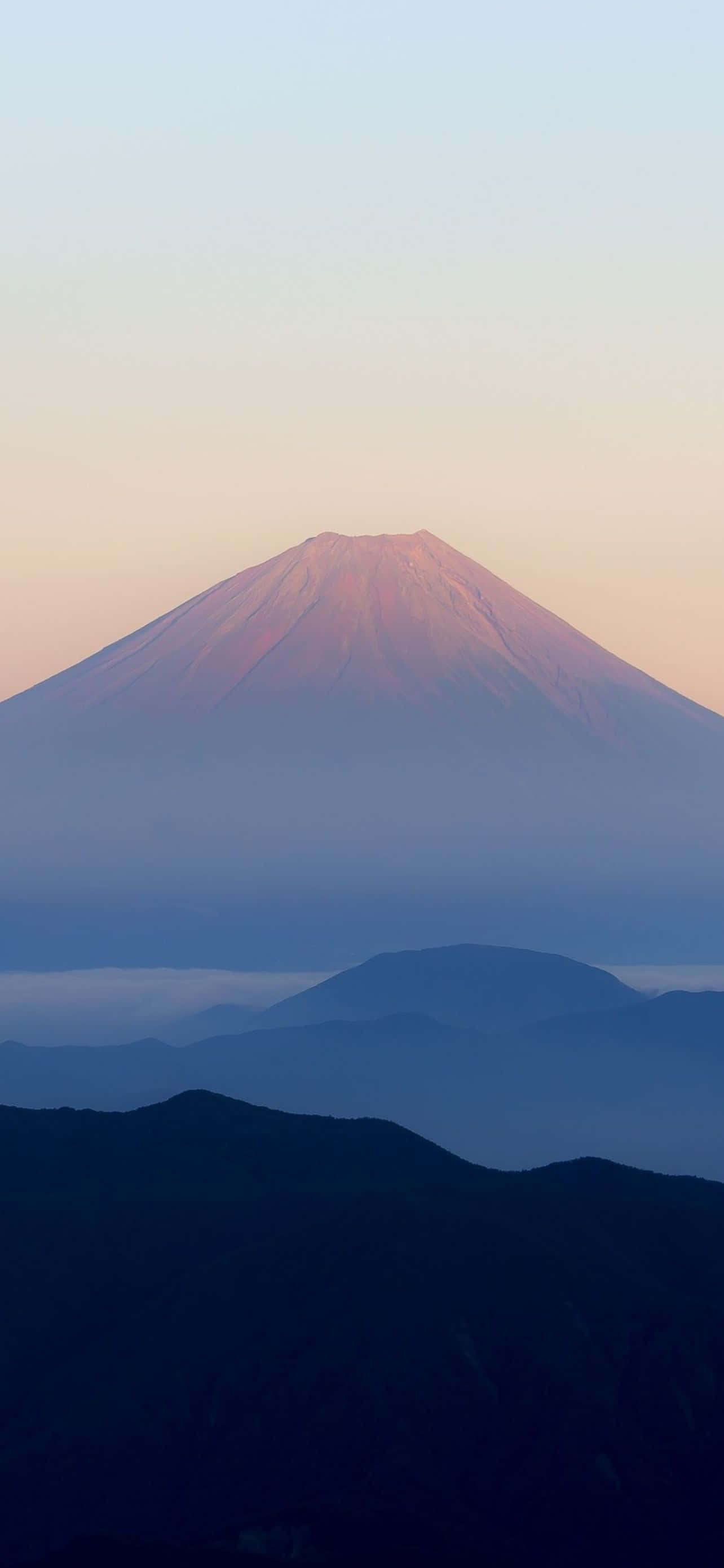 Mountain iPhone 桌布 壁紙 — 富士山沐浴在柔和的粉紅和藍色黎明光中，下方是層層疊疊的霧氣山脈。