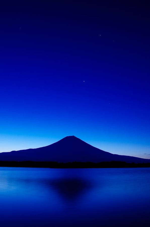 dark blue aesthetic tumblr 桌布 壁紙 — 富士山的剪影在平靜的水面上倒映，頭上是星光閃爍、深藍發亮的暮色天空。