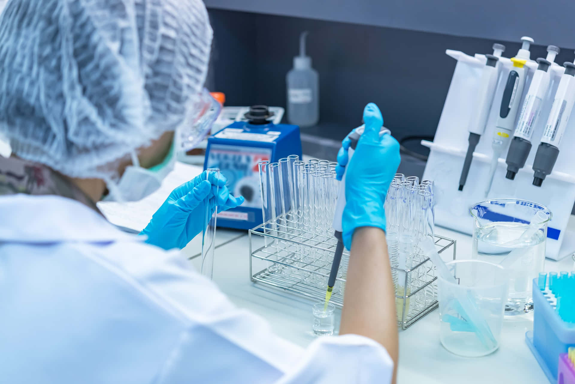 科學 桌布 壁紙 — 實驗室裡，一位科學家小心翼翼地用移液器將液體轉移到試管中，周圍是玻璃器皿和設備。
