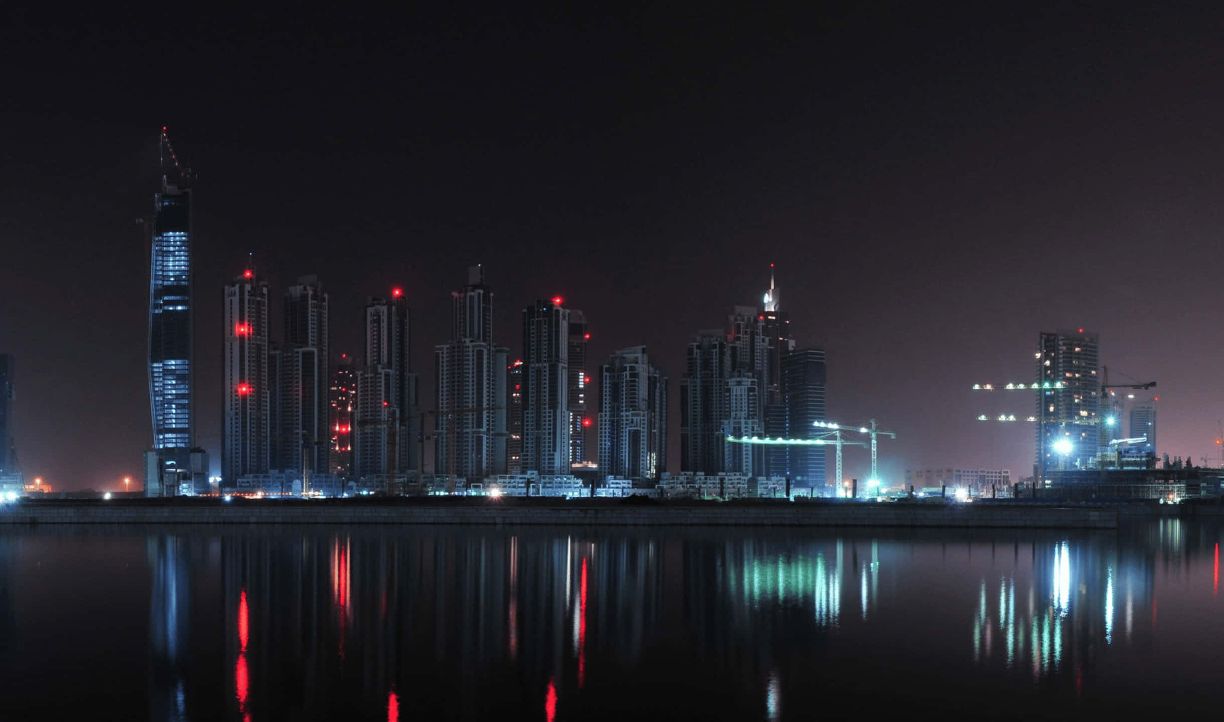 City Skyline 桌布 壁紙 — 寧靜水面上倒映著紅色建築燈光的摩天大樓夜景。