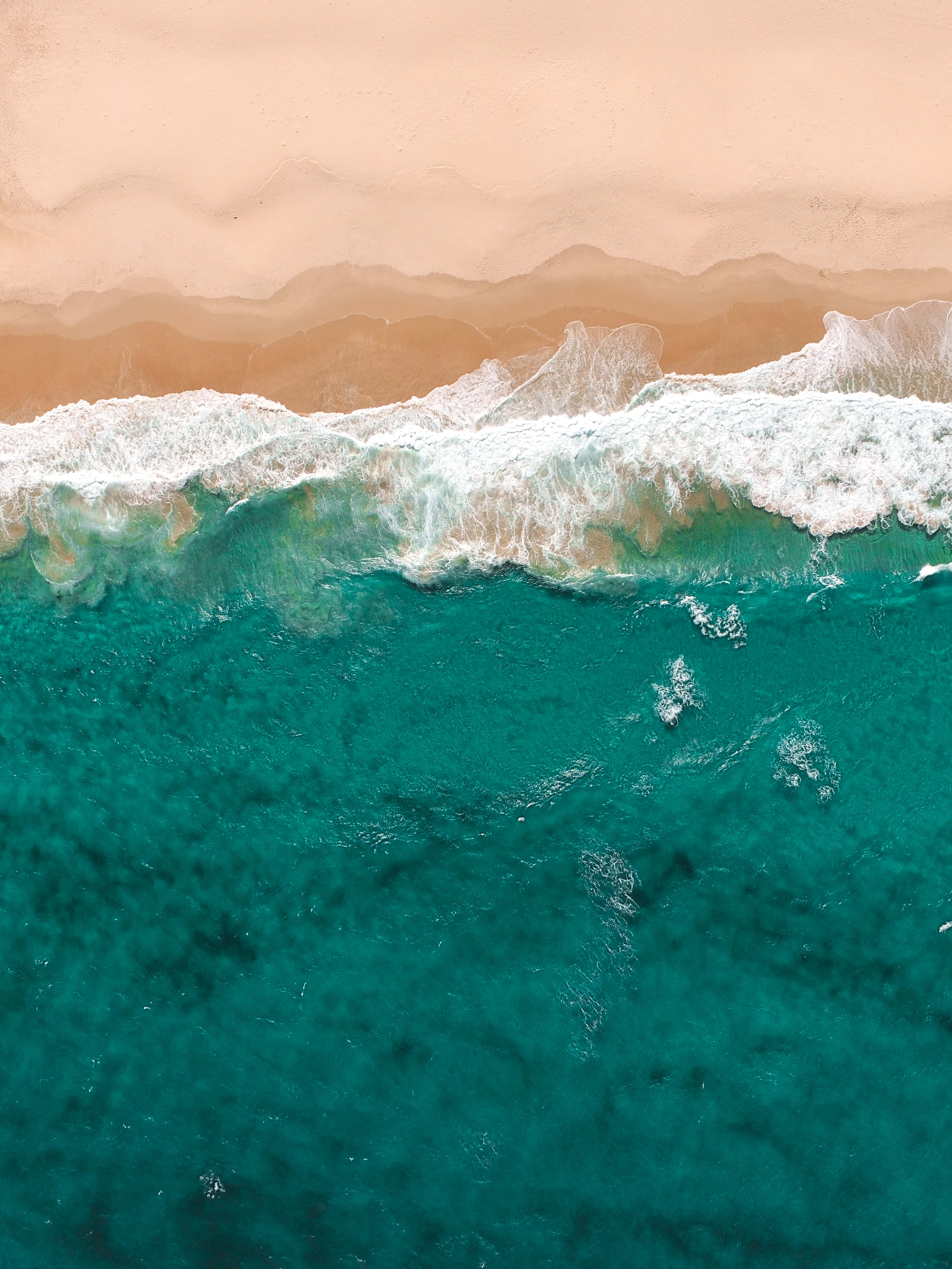 Ocean Aesthetic Phone 桌布 壁紙 — 寧靜海岸場景中，綠松石色的海浪拍打著桃色沙灘的鳥瞰圖。