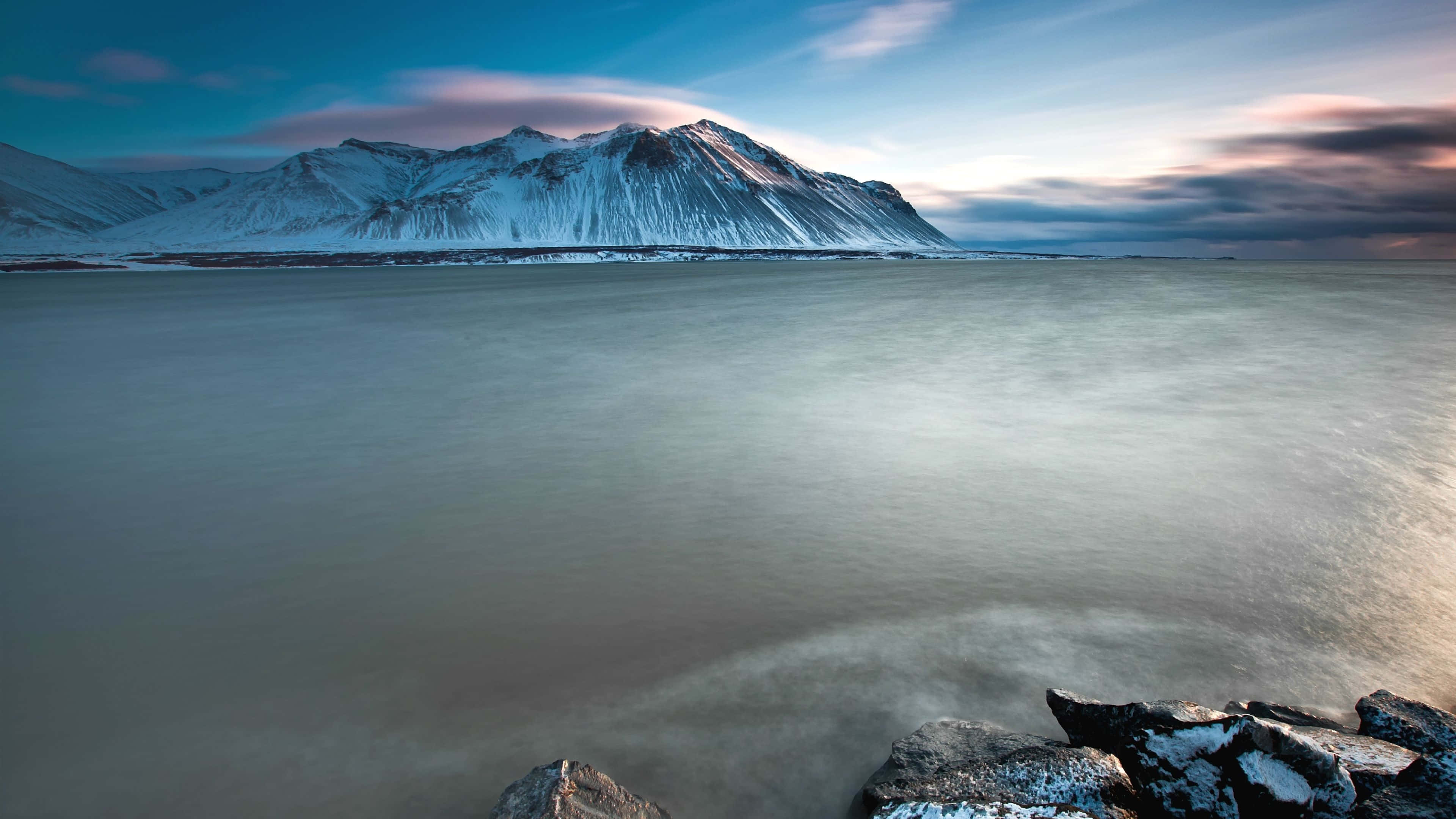 Iceland Desktop 桌布 壁紙 — 寧靜的冬季景觀，白雪覆蓋的山脈在平靜的水面上倒映，柔和暮色天空下。