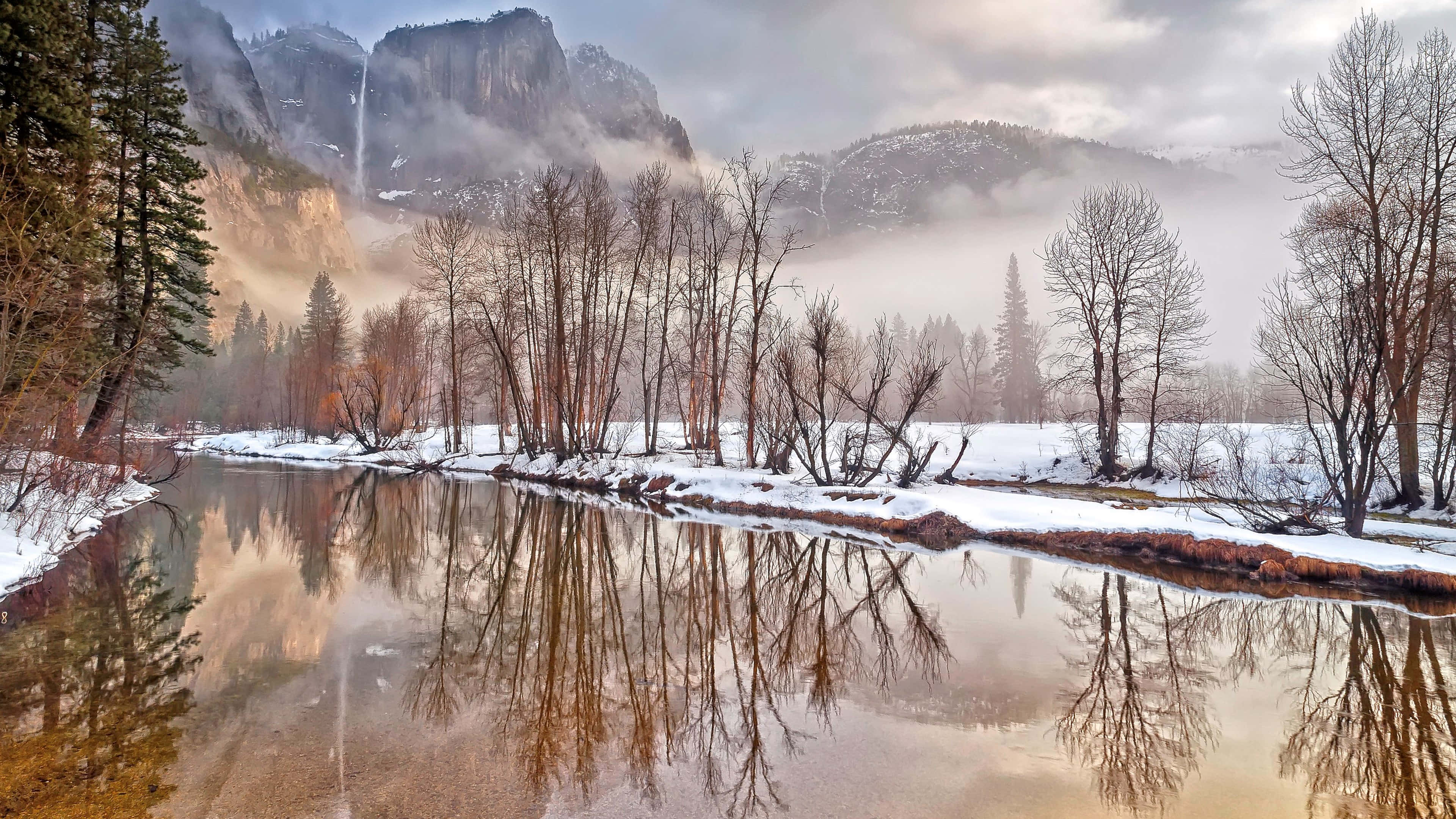 Winter Scenery Desktop 桌布 壁紙 — 寧靜的冬季景觀，白雪覆蓋的樹木和一條平靜的河流，倒映著霧濛濛的山脈和傾瀉而下的瀑布。