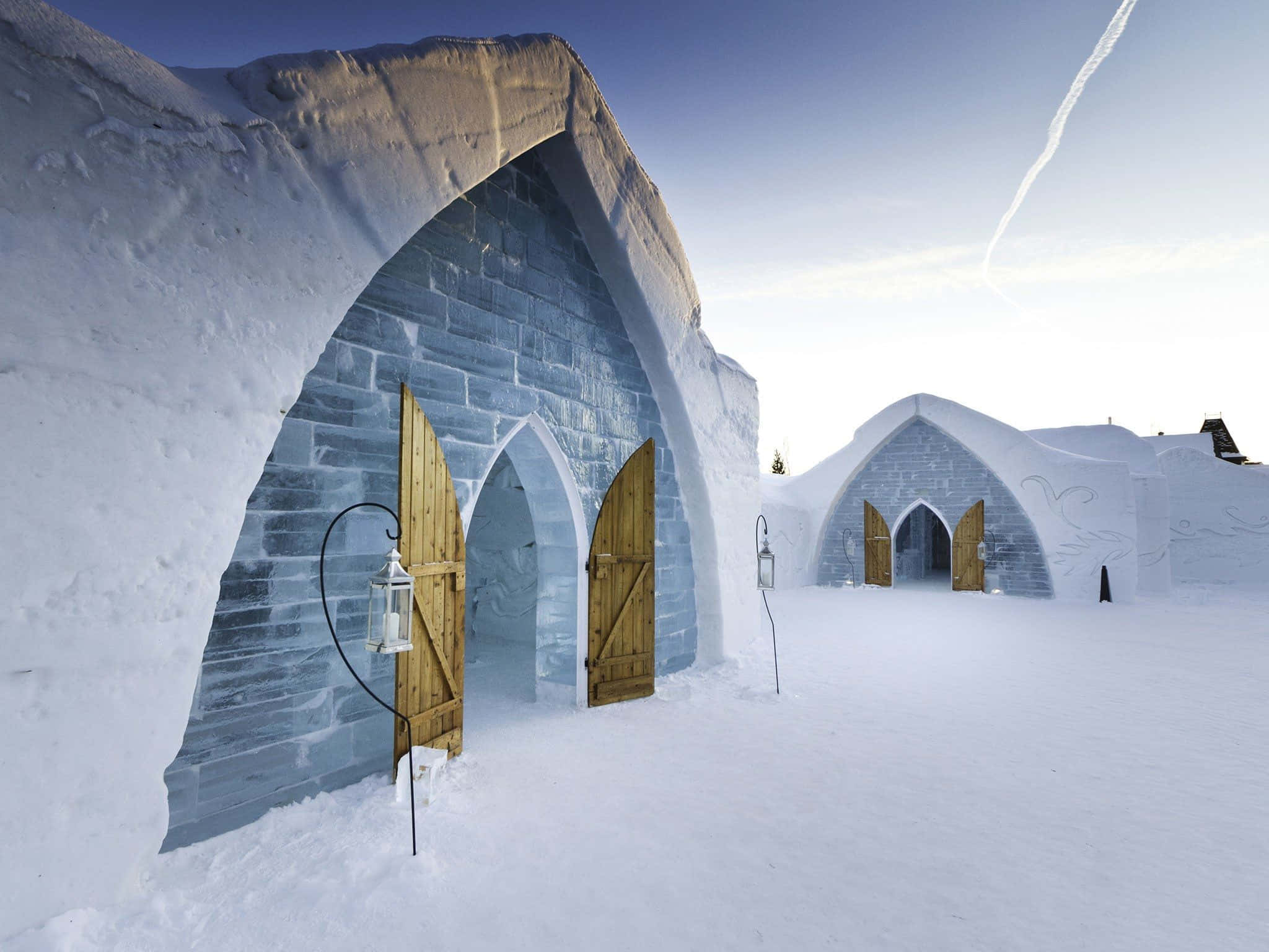 Ice Hotel 桌布 壁紙 — 寧靜的冬日場景，冰屋配有木門和燈籠，在清澈的藍天下。