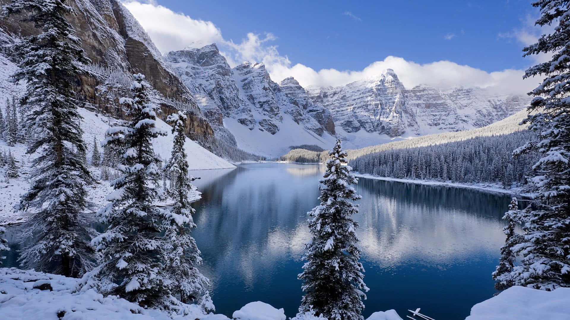 Best Winter 桌布 壁紙 — 寧靜的冬日湖面映照著白雪覆蓋的山巒和常青樹，天空湛藍，白雲朵朵。