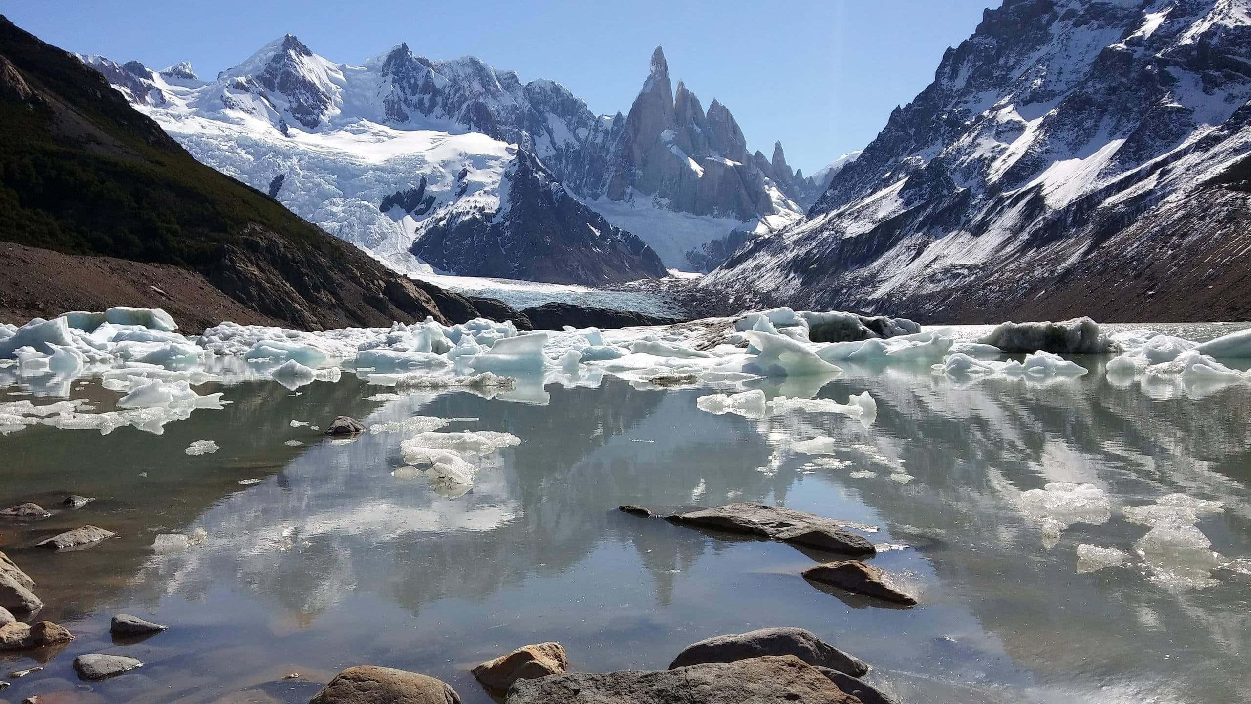 Patagonia 桌布 壁紙 — 寧靜的冰川湖上散落著浮冰，在清澈的藍天下映照著白雪覆蓋的山峰。