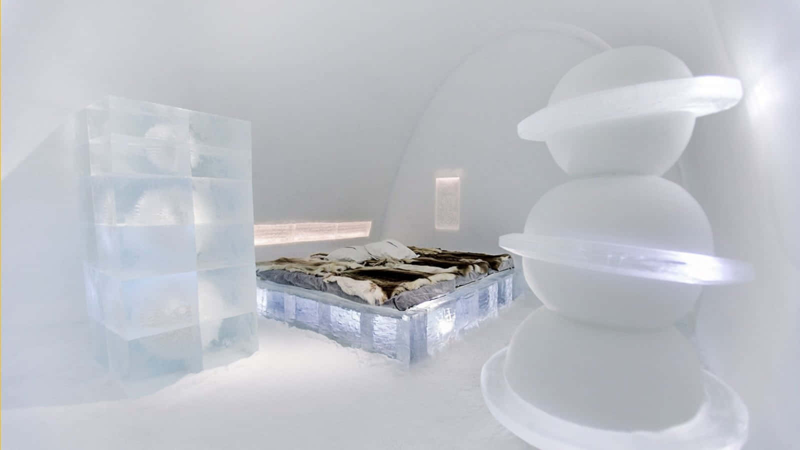 Ice Hotel 桌布 壁紙 — 寧靜的冰酒店房間，配有毛毯床和發光的冰製家具，在柔和的白光下。