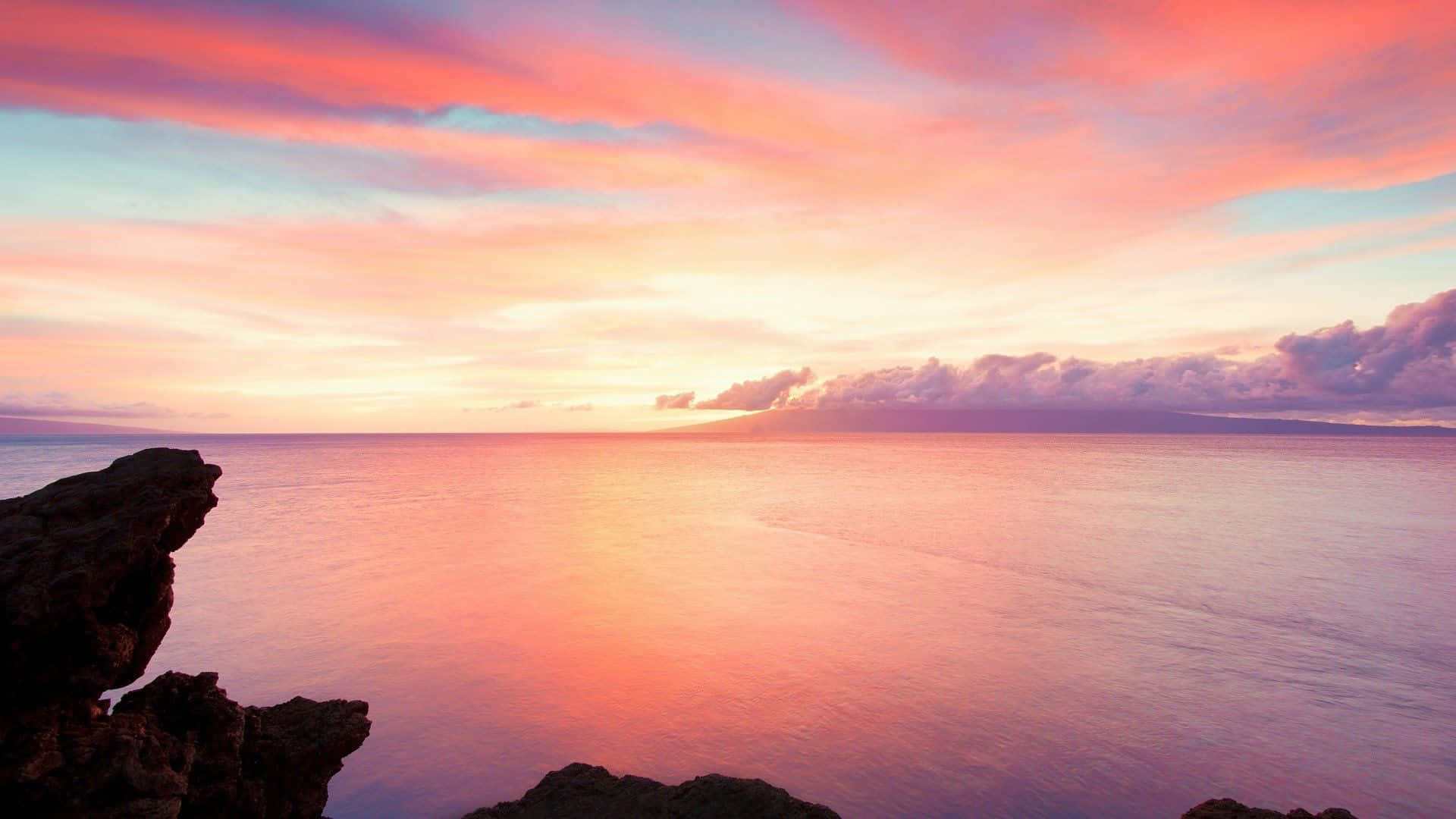 Calm Aesthetic Desktop 桌布 壁紙 — 寧靜的夕陽將海洋染成火熱的粉紅色和橙色，深色的岩石框住了平靜的地平線。