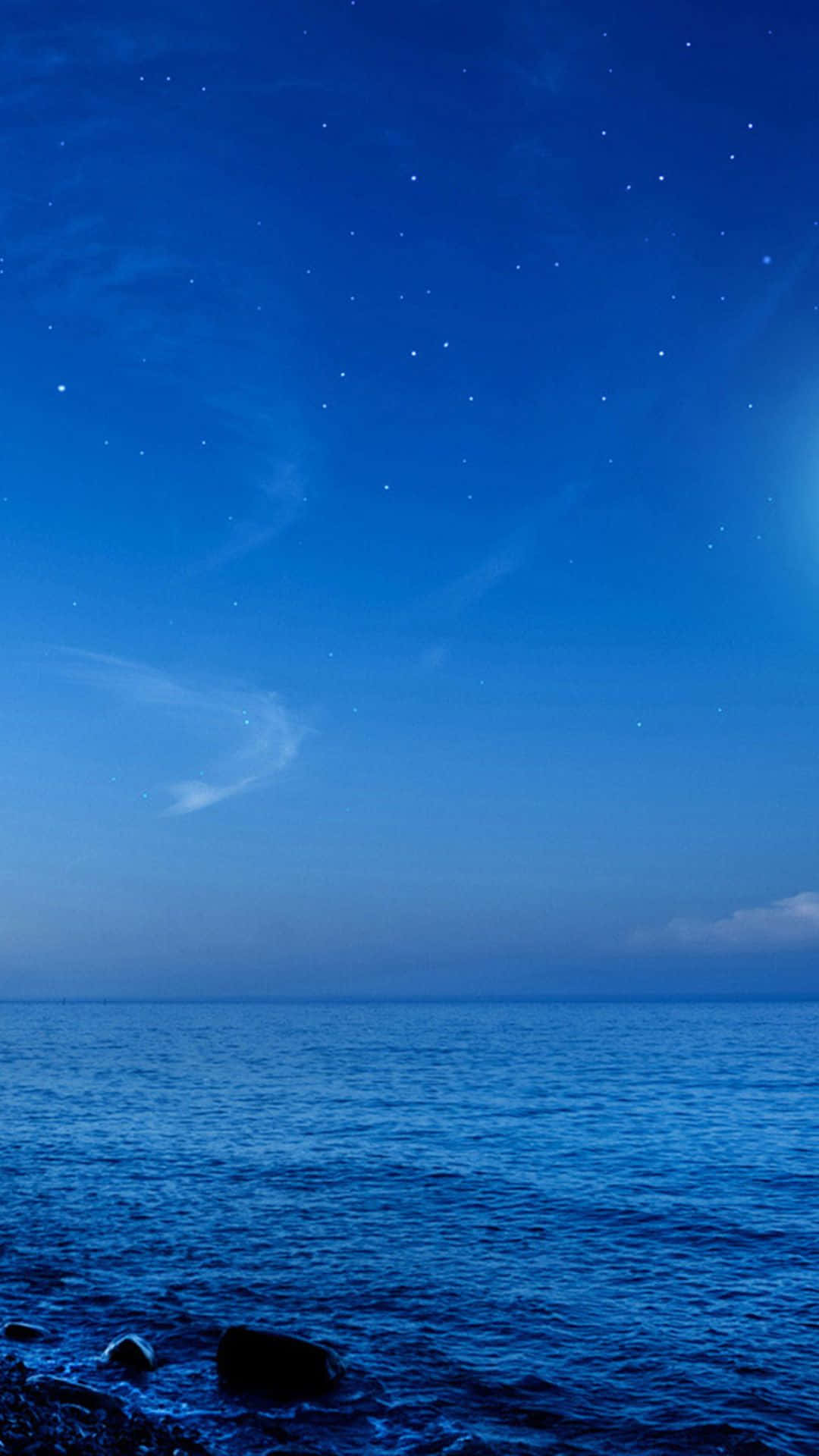 Galaxy S5 桌布 壁紙 — 寧靜的夜晚場景，繁星點點的深藍色天空下，平靜的海洋與岩石海岸相接。