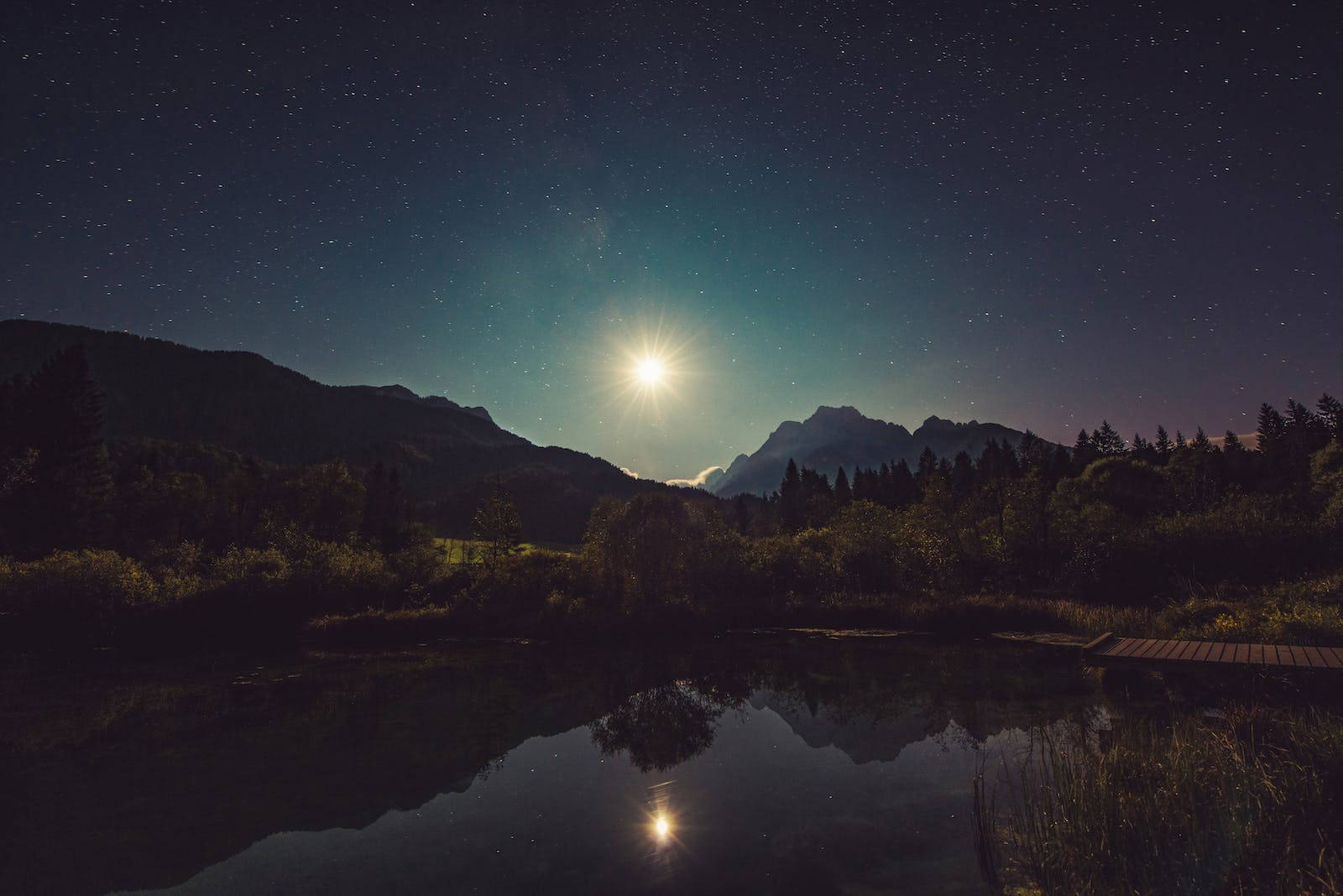 月亮桌面 桌布 壁紙 — 寧靜的夜景，明亮的月亮在山上閃耀，倒映在被樹木環繞的平靜湖面上。