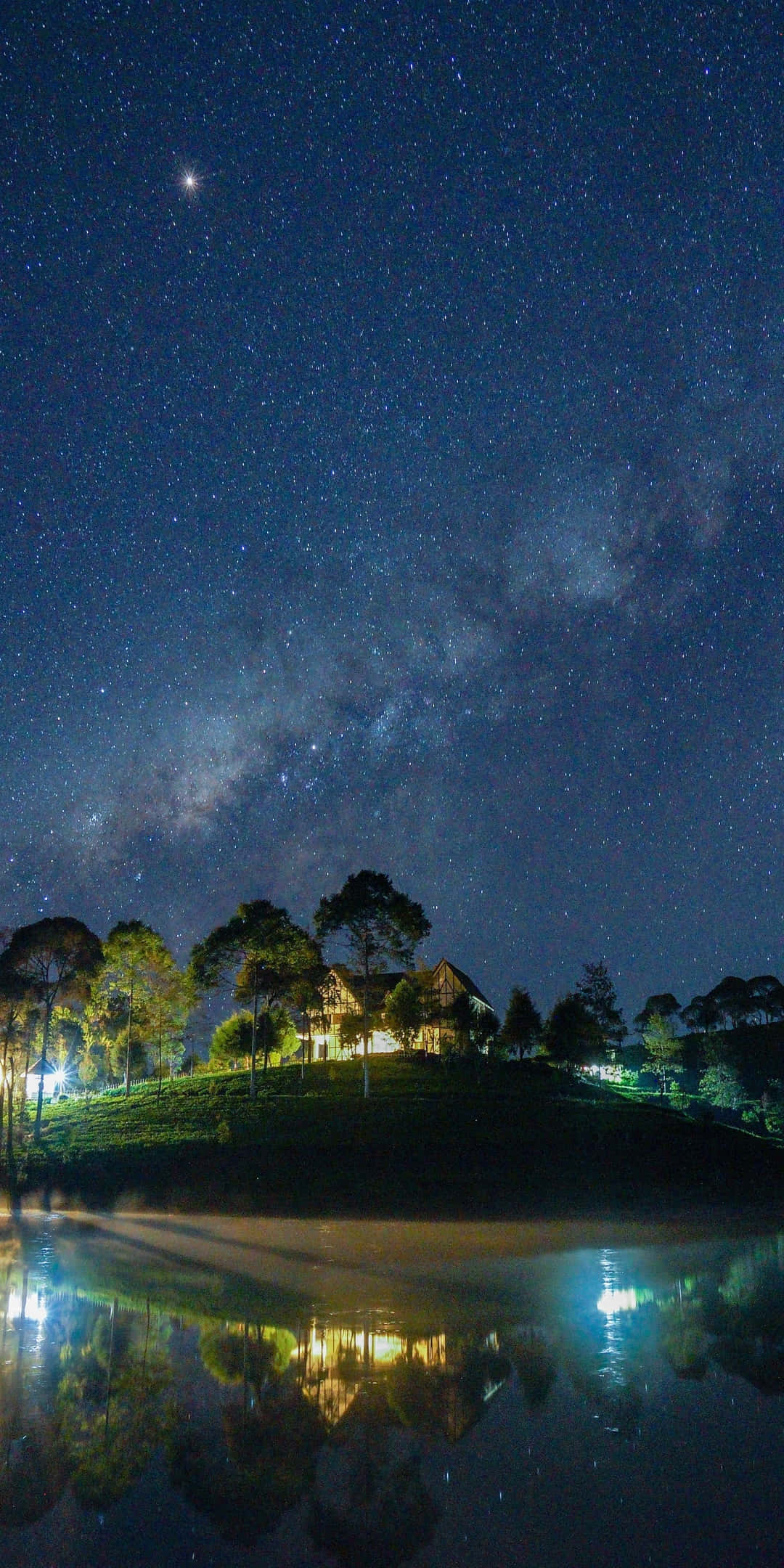 自然 桌布 壁紙 — 寧靜的夜景，星空和銀河拱在發光的房子上，倒映在平靜的水面上。