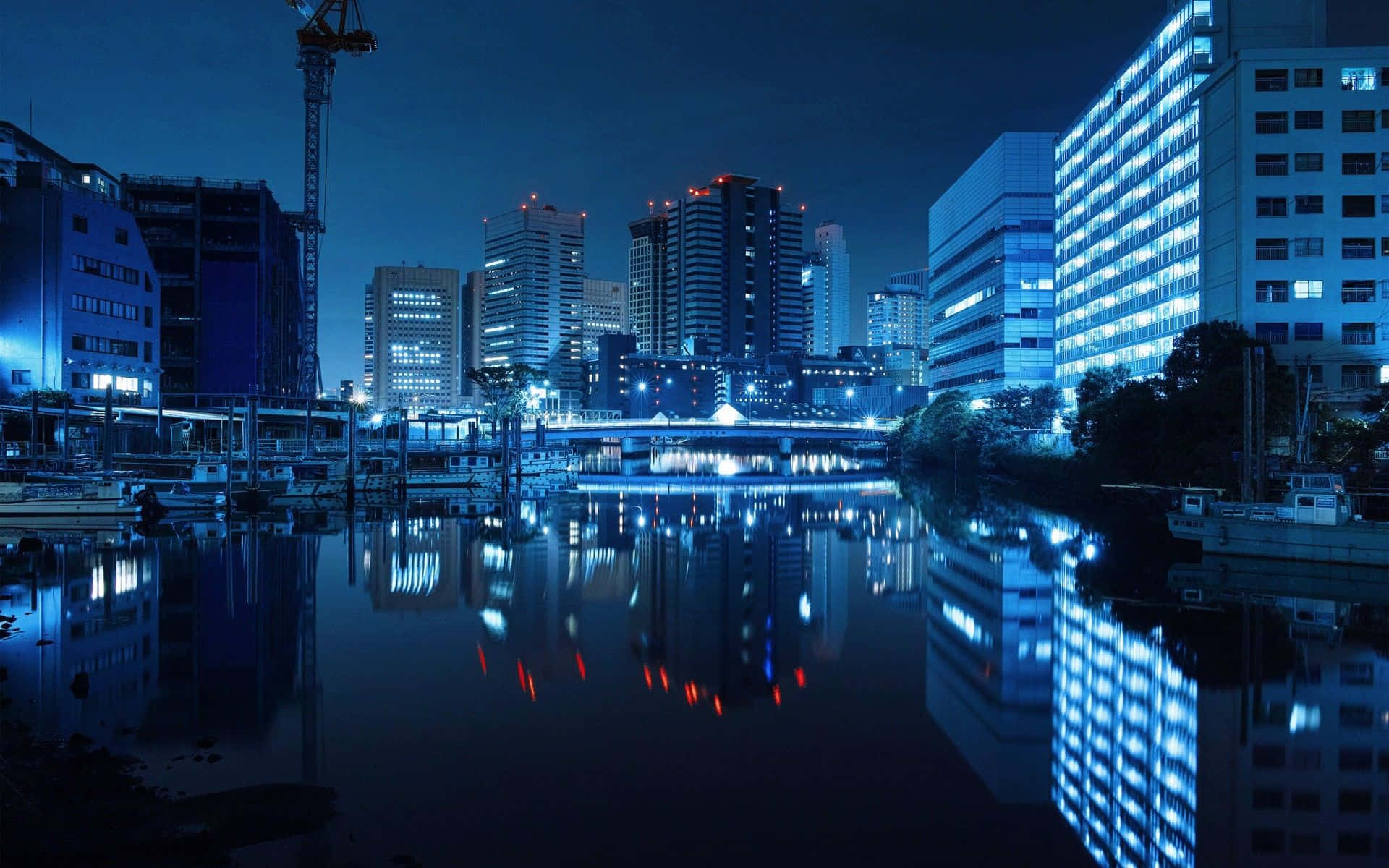 夜晚城市天際線倒映在平靜的河流中，有發光的建築物和橋樑。 — 東京迷幻 sessions 壁紙