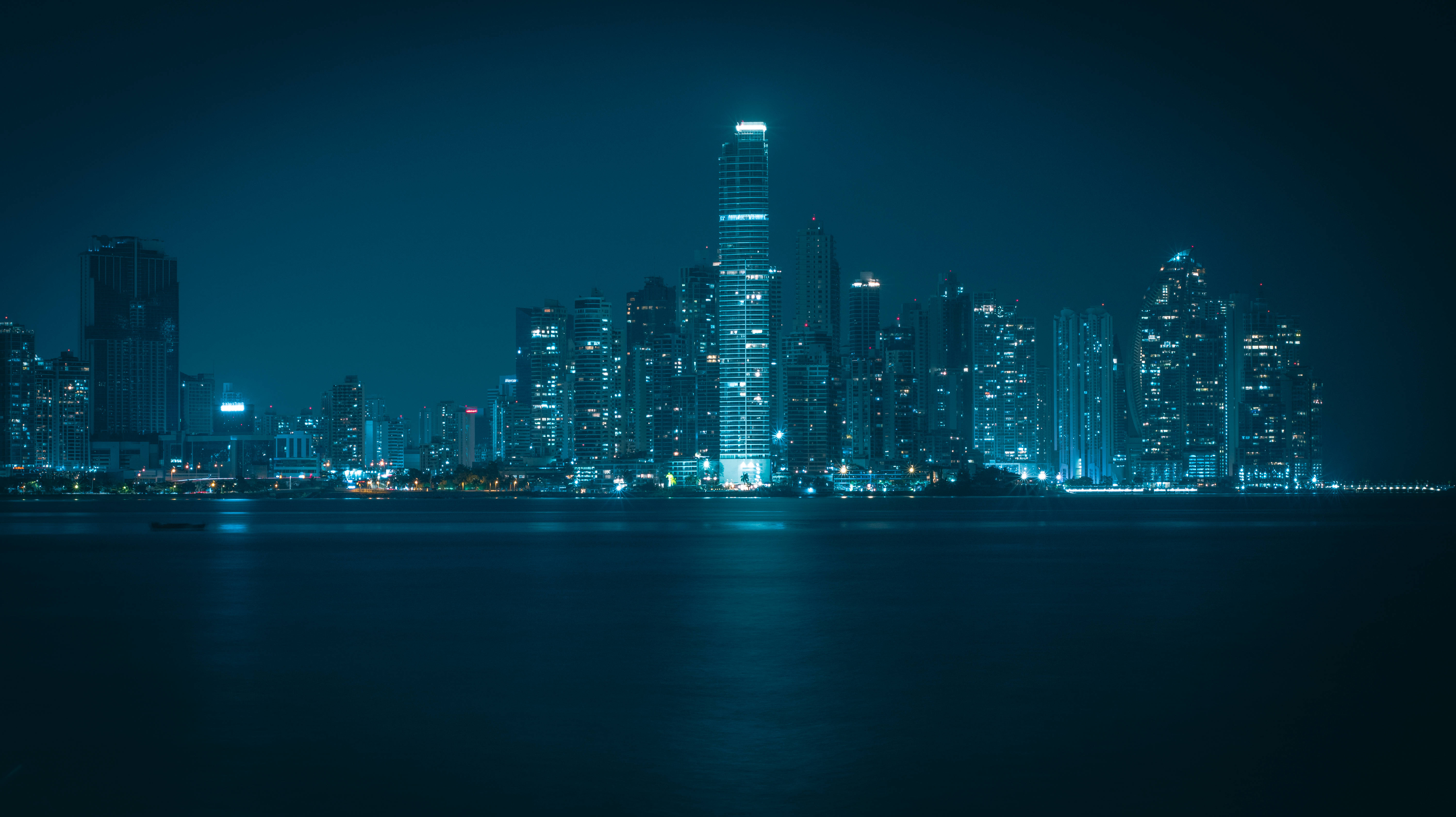 Panama 桌布 壁紙 — 寧靜的夜景城市景觀，在深藍色天空下，發光的摩天大樓倒映在平靜的水面上。