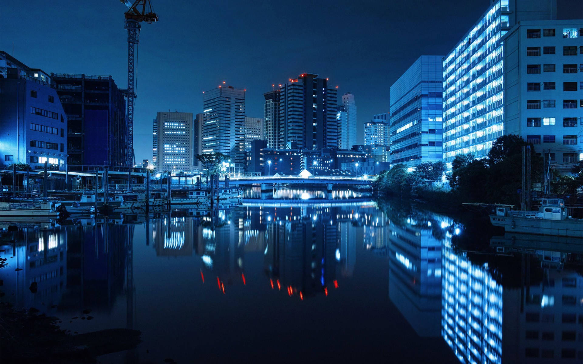 Unique HD 桌布 壁紙 — 寧靜的夜景城市景觀，閃爍的摩天大樓和一條平靜的河流反射出它們的藍色和紅色燈光。