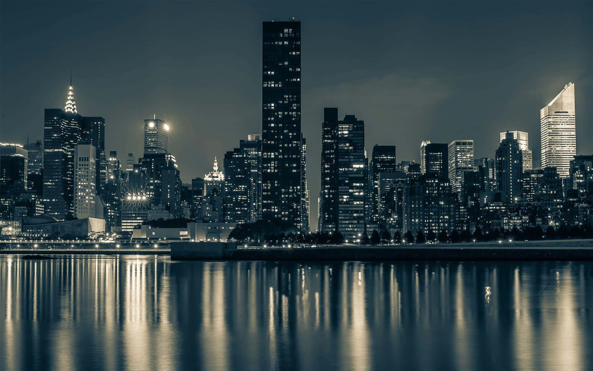 紐約市 桌布 壁紙 — 寧靜的夜景城市景觀，高聳的摩天大樓在黑暗的天空下倒映在平靜的水面上。