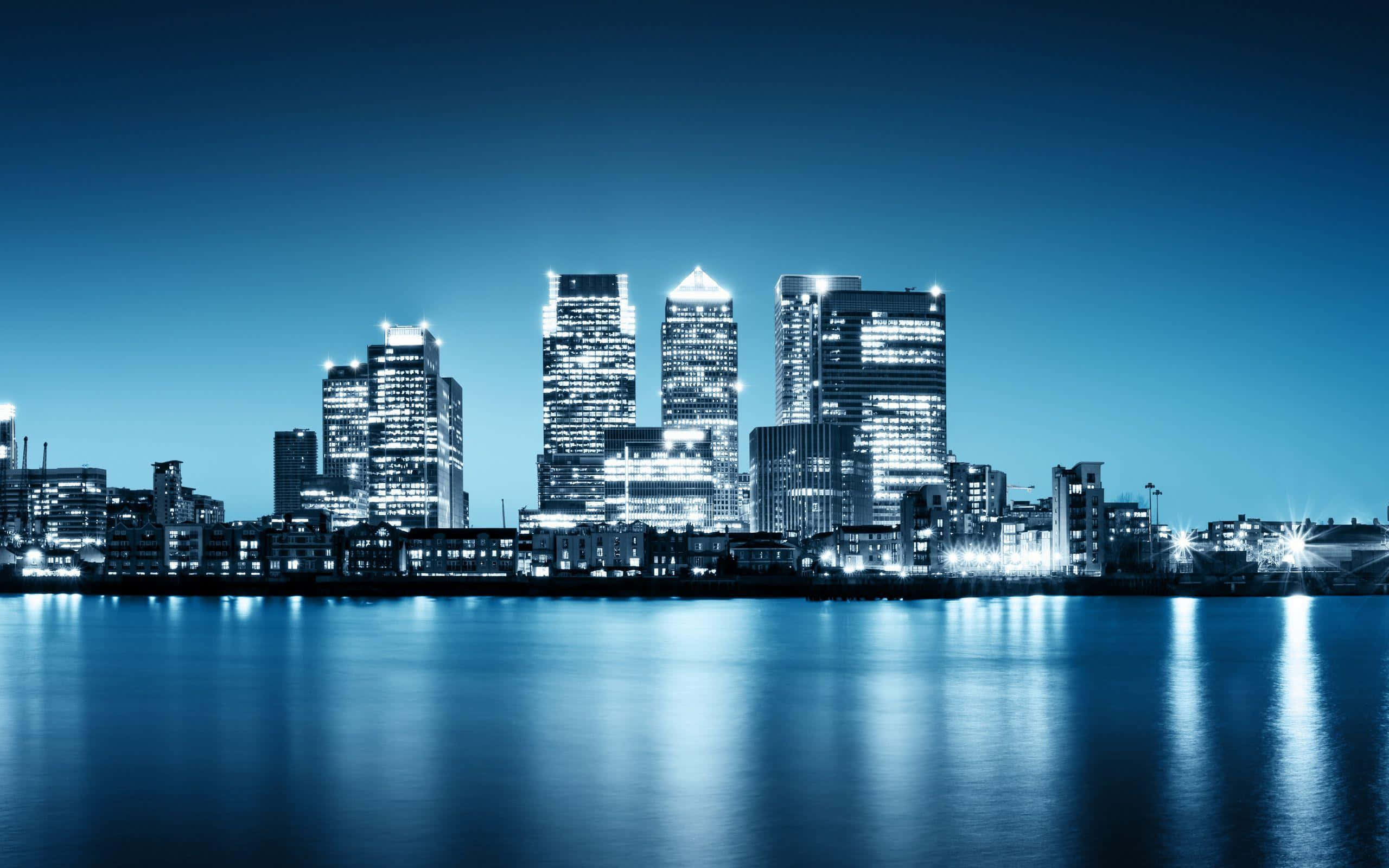 3d City 桌布 壁紙 — 寧靜的夜景城市景觀，高聳的摩天大樓在深藍色天空下倒映在平靜的水面上。