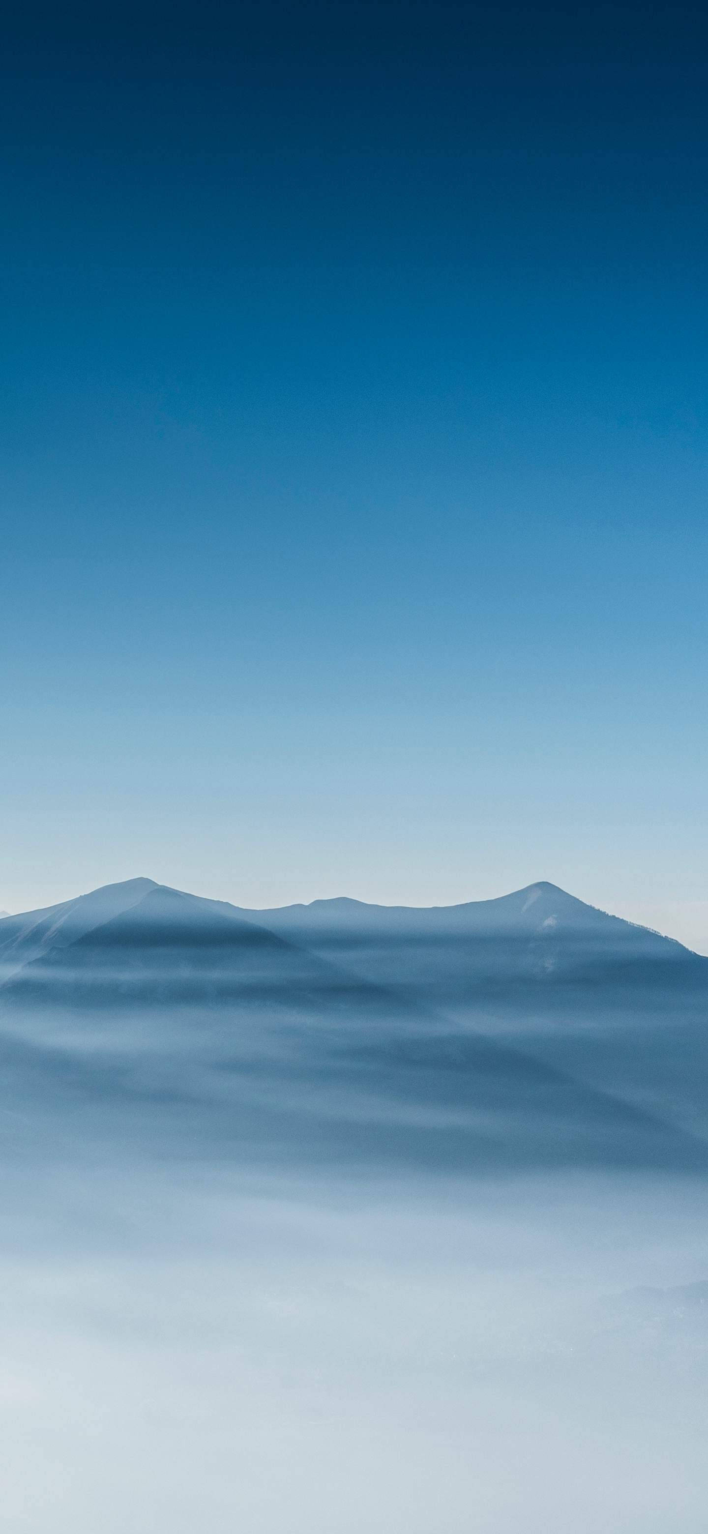  壁紙 — 寧靜的山峰在漸變藍天下從霧海中升起。