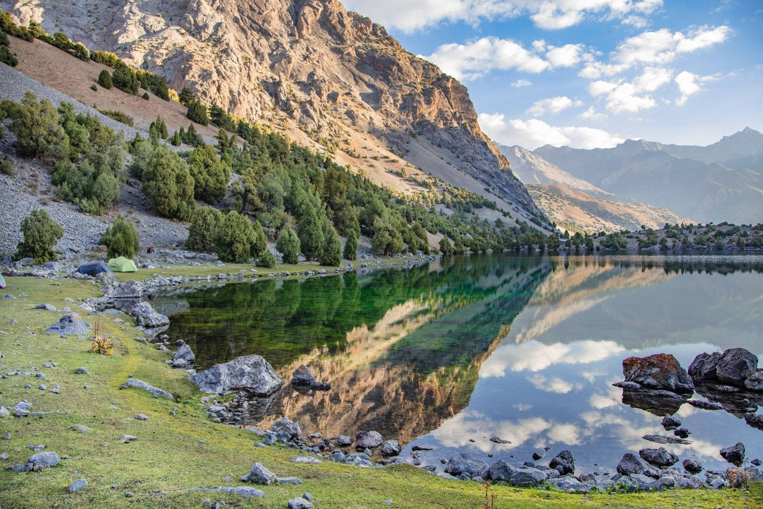 Tajikistan 桌布 壁紙 — 寧靜的山湖映照著崎嶇的懸崖和蓬鬆的雲朵，在明亮的藍天下。