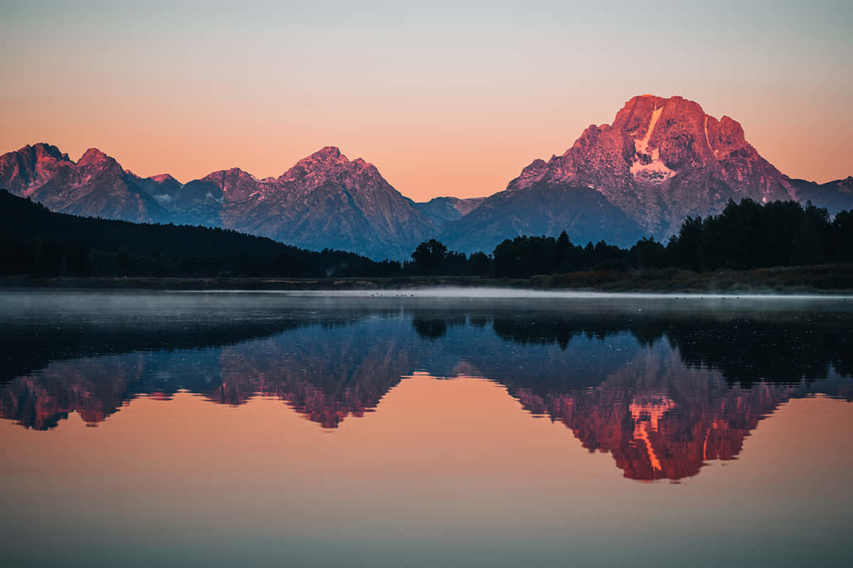 reflection 桌布 壁紙 — 寧靜的山湖映照著日出時閃耀粉紅和橙色的雄偉山峰。