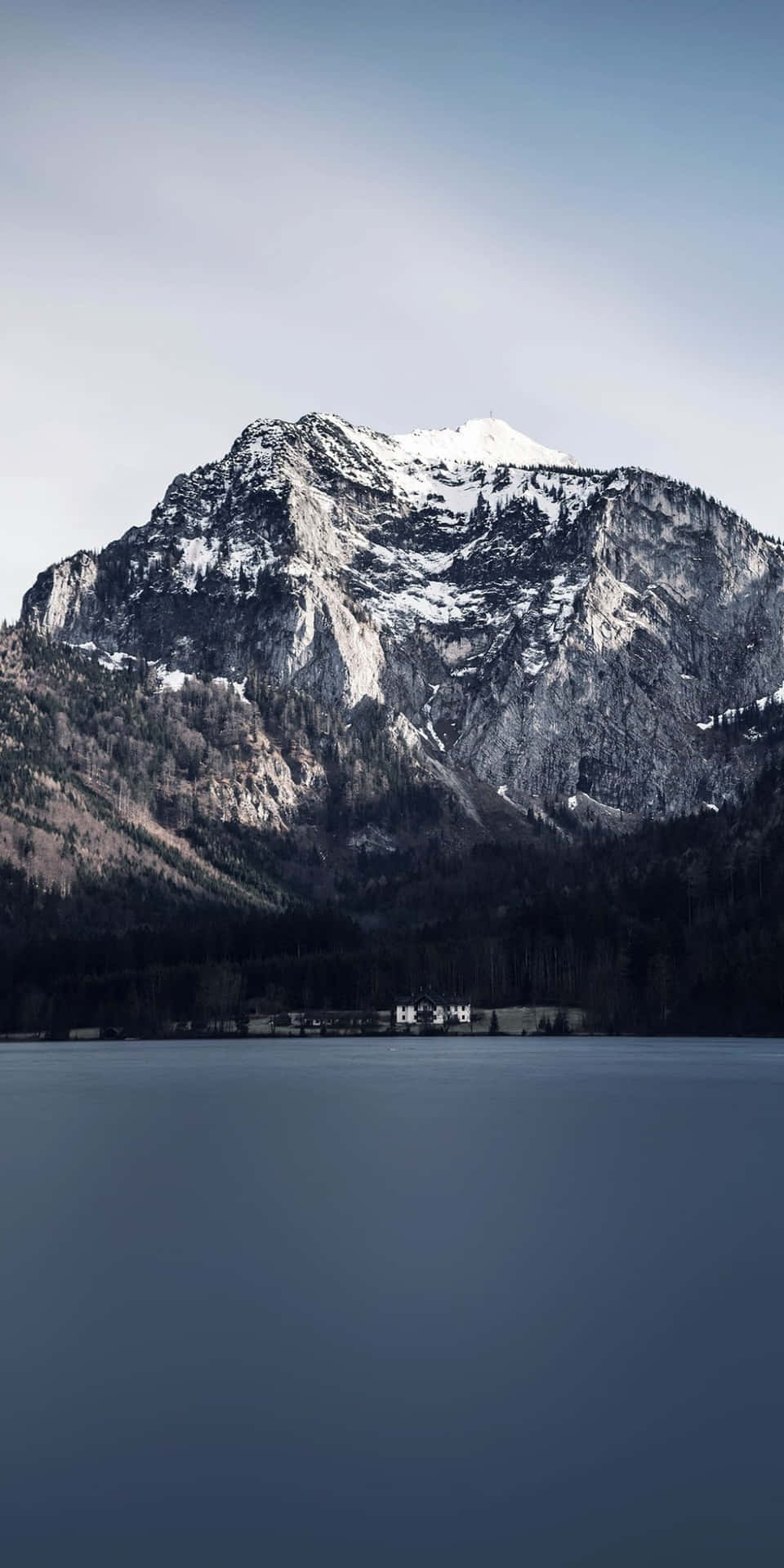  壁紙 — 寧靜的山湖映照著雪峰，蒼白的天空下，岸邊有一座小建築。